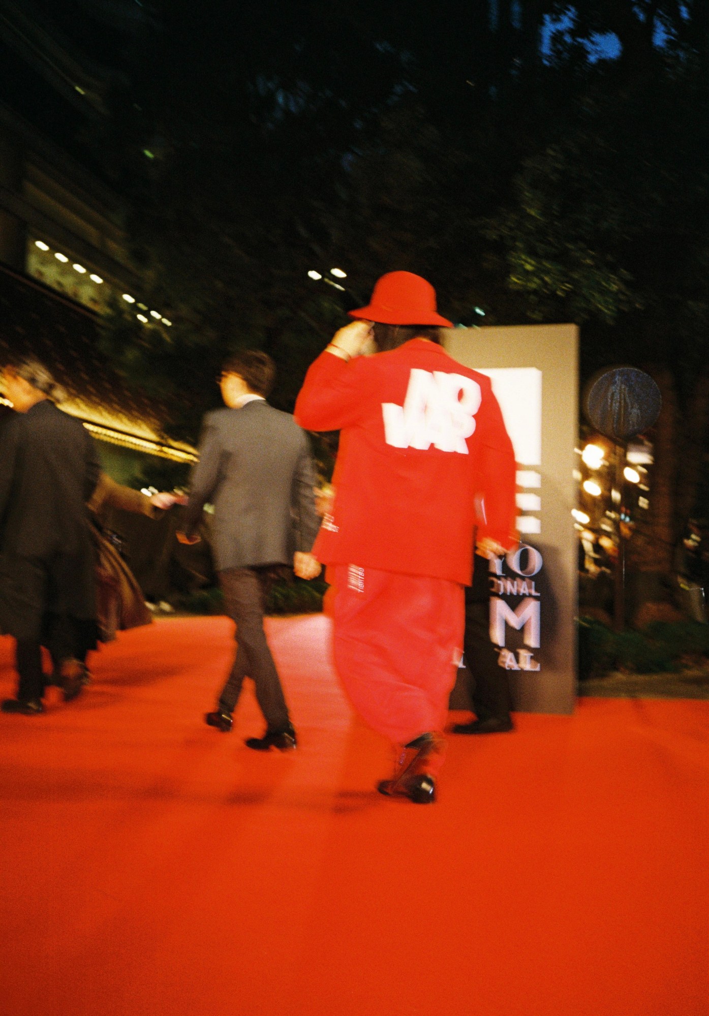 a blurry image of a man shot from behind in a red tracksuit with the slogan 'no war', on a red carpet