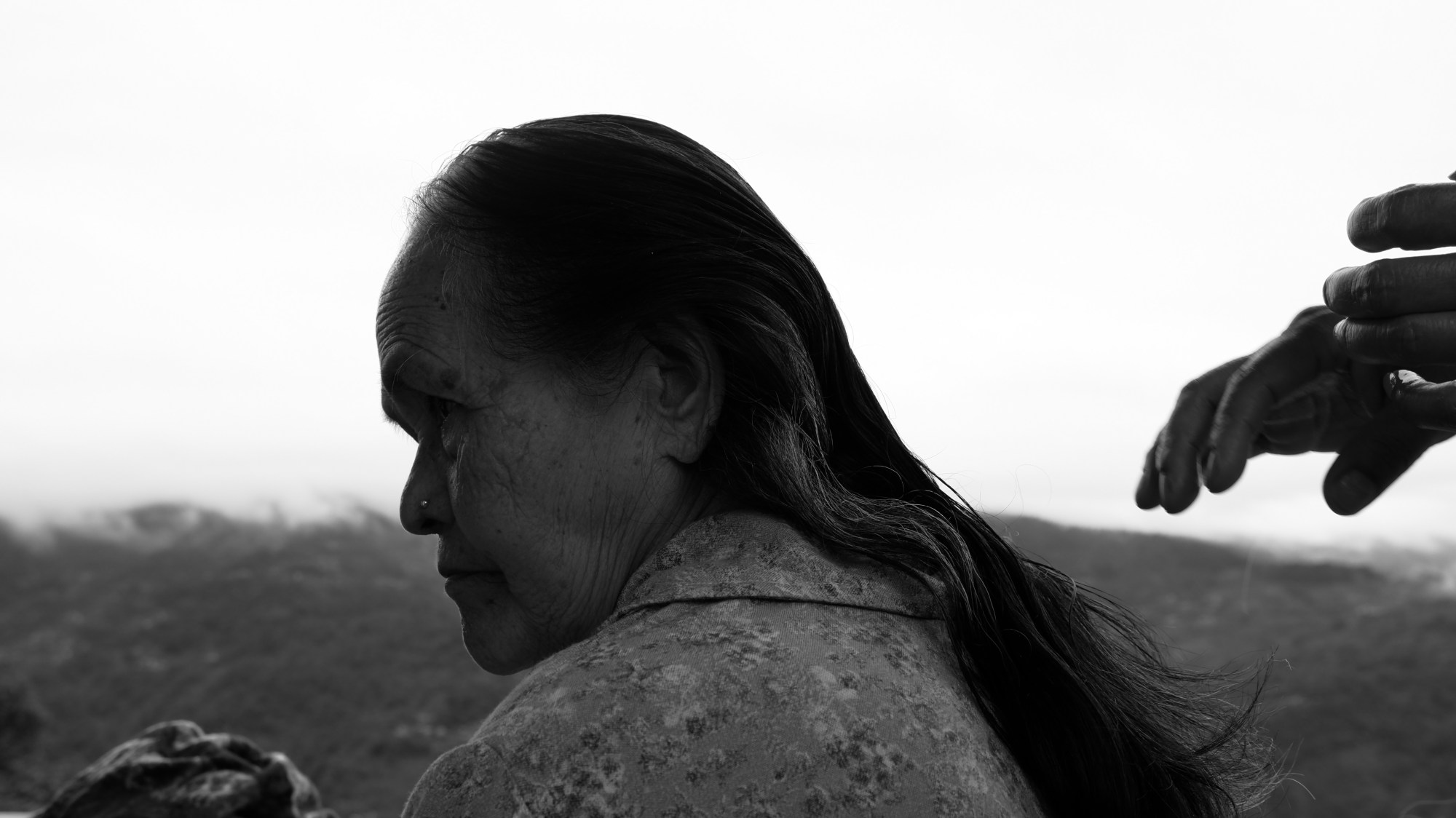 black-and-white image of an old woman seen in profile, hands about to begin doing her hair