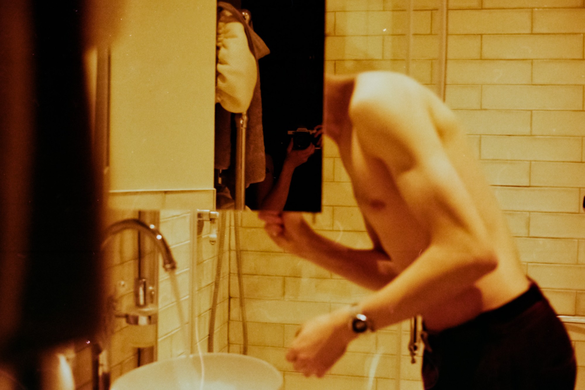 a sepia-toned image of a topless man in the bathroom, his head cut off by the cabinet door