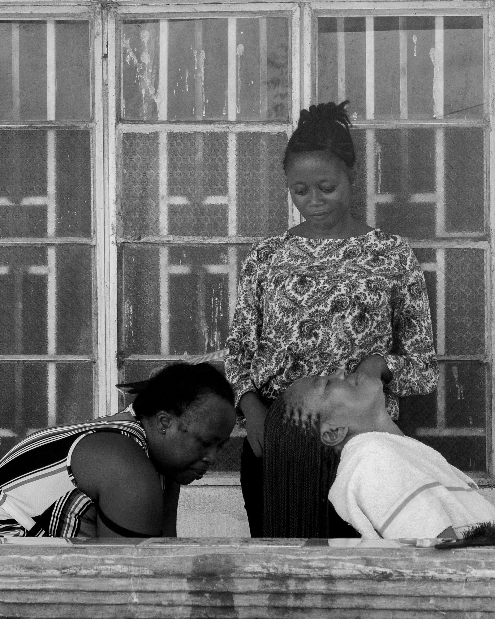 black-and-white image of a woman having her braids dipped by two women hairdressers