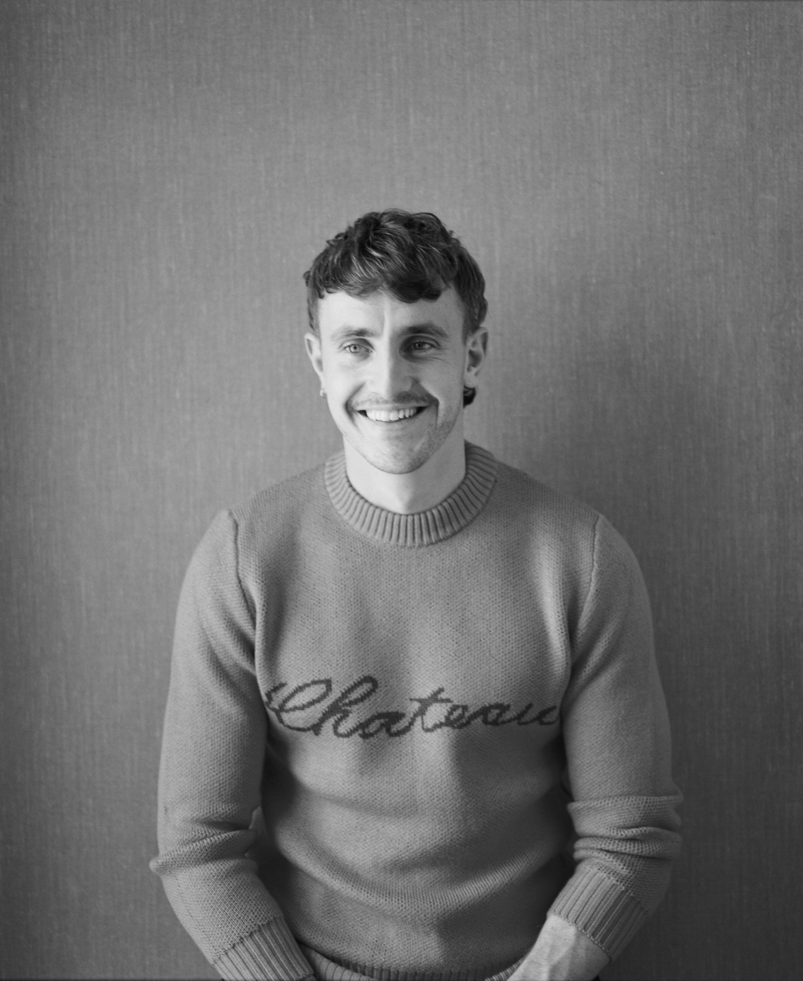 a black and white photo of paul wearing a jumper that reads 'chateau'