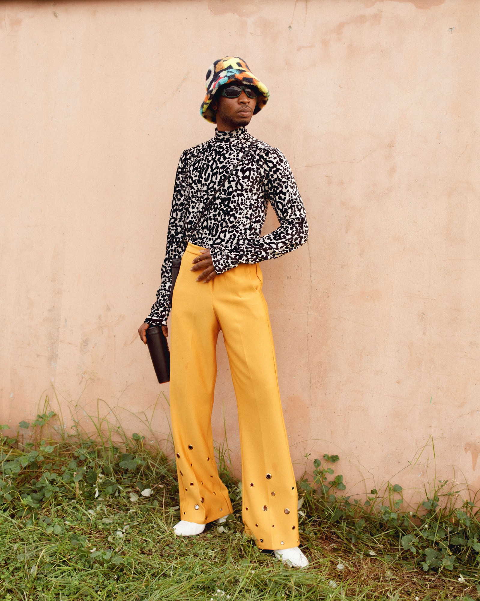 A man wearing a colourful outfit, stood against a wall