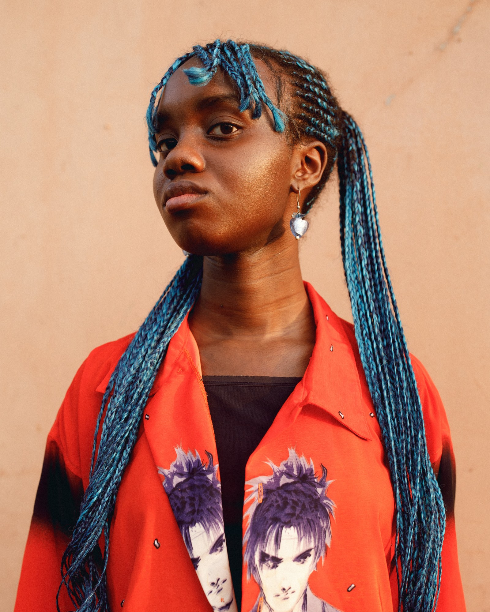 A woman with blue braids in a wide-lapelled orange jacket with illustrations on it