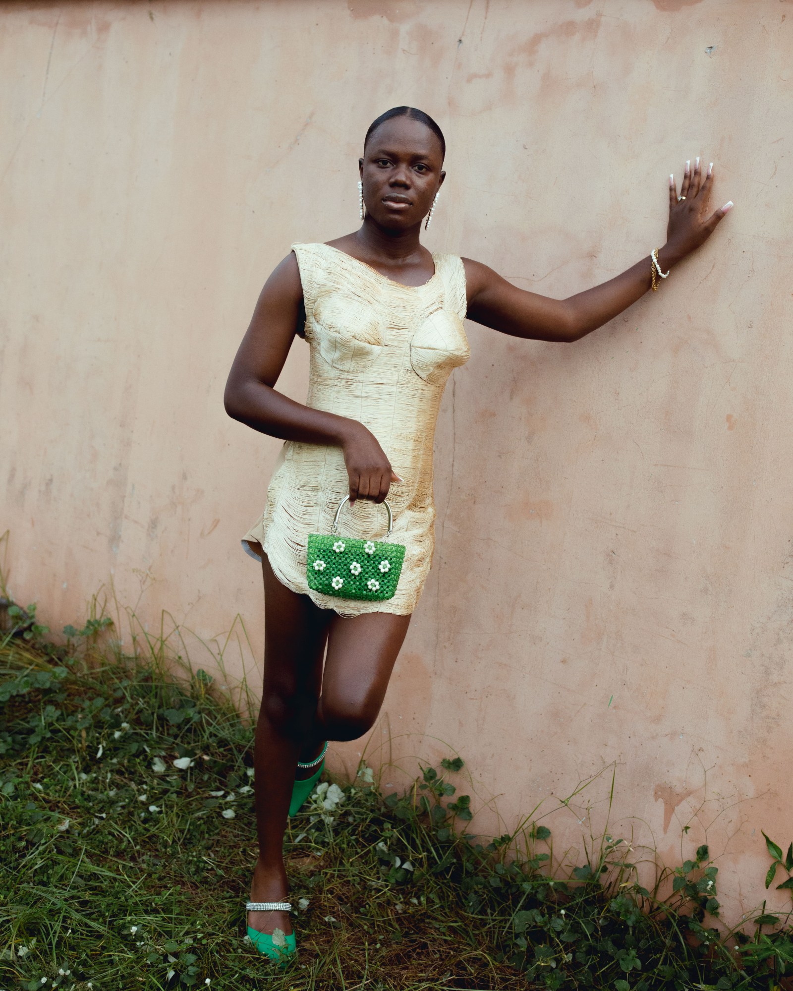 A woman stood against a beige wall in a gold minidress and a beaded bag