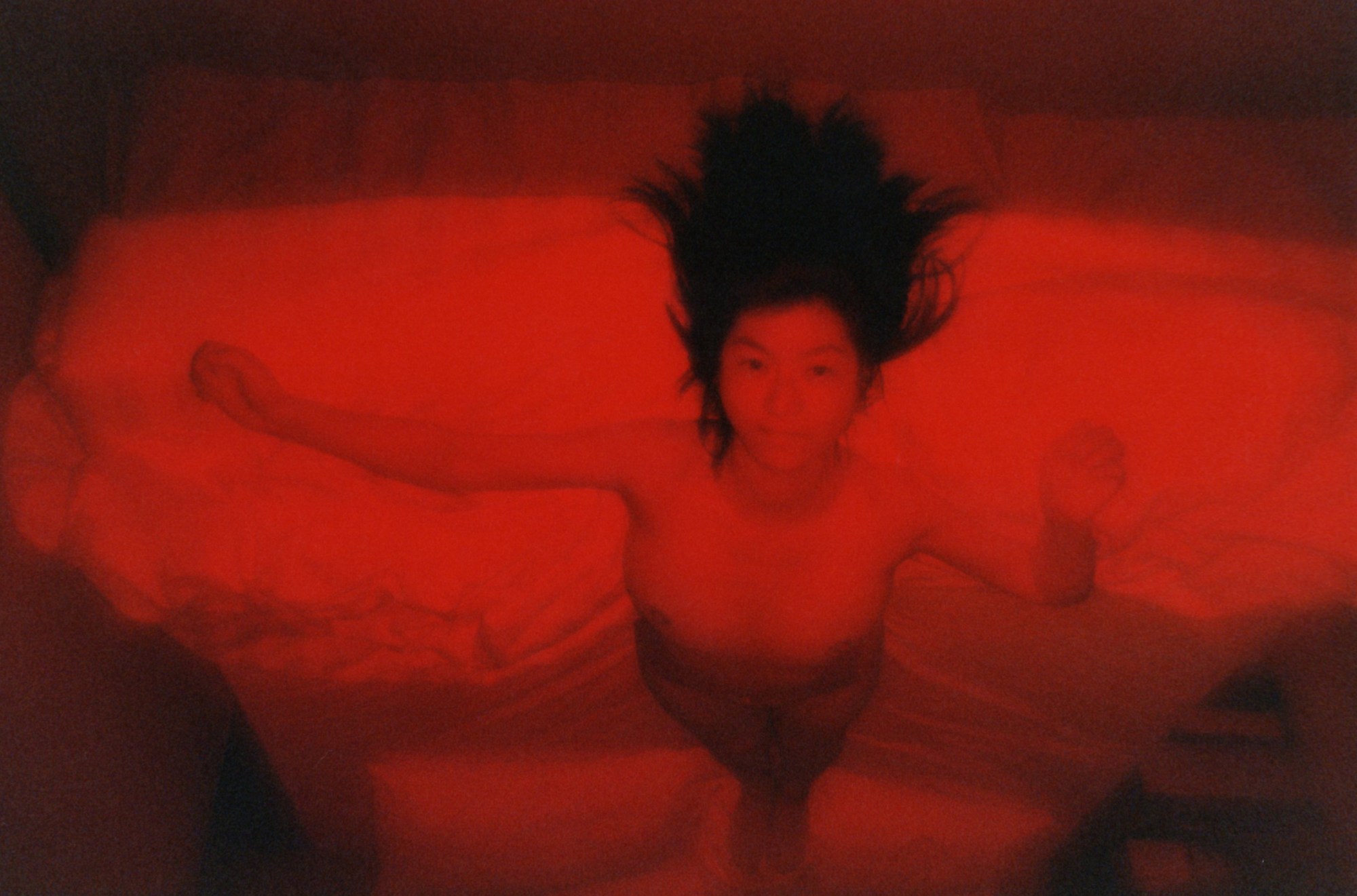 A woman staring into the camera while lying upside down on a bed covered in white sheets