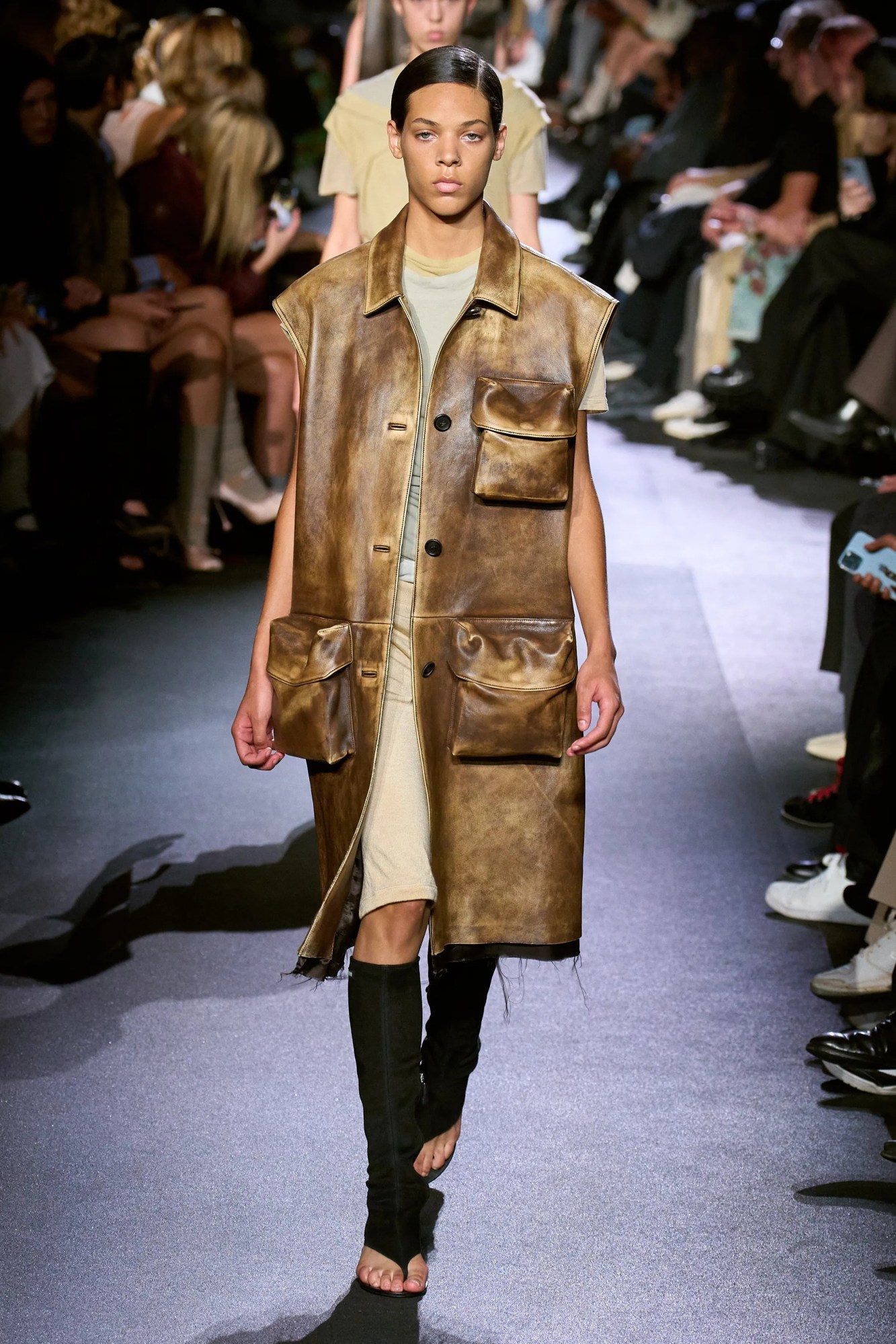 A model walking the Miu Miu SS23 runway in a worn brown leather vest coat