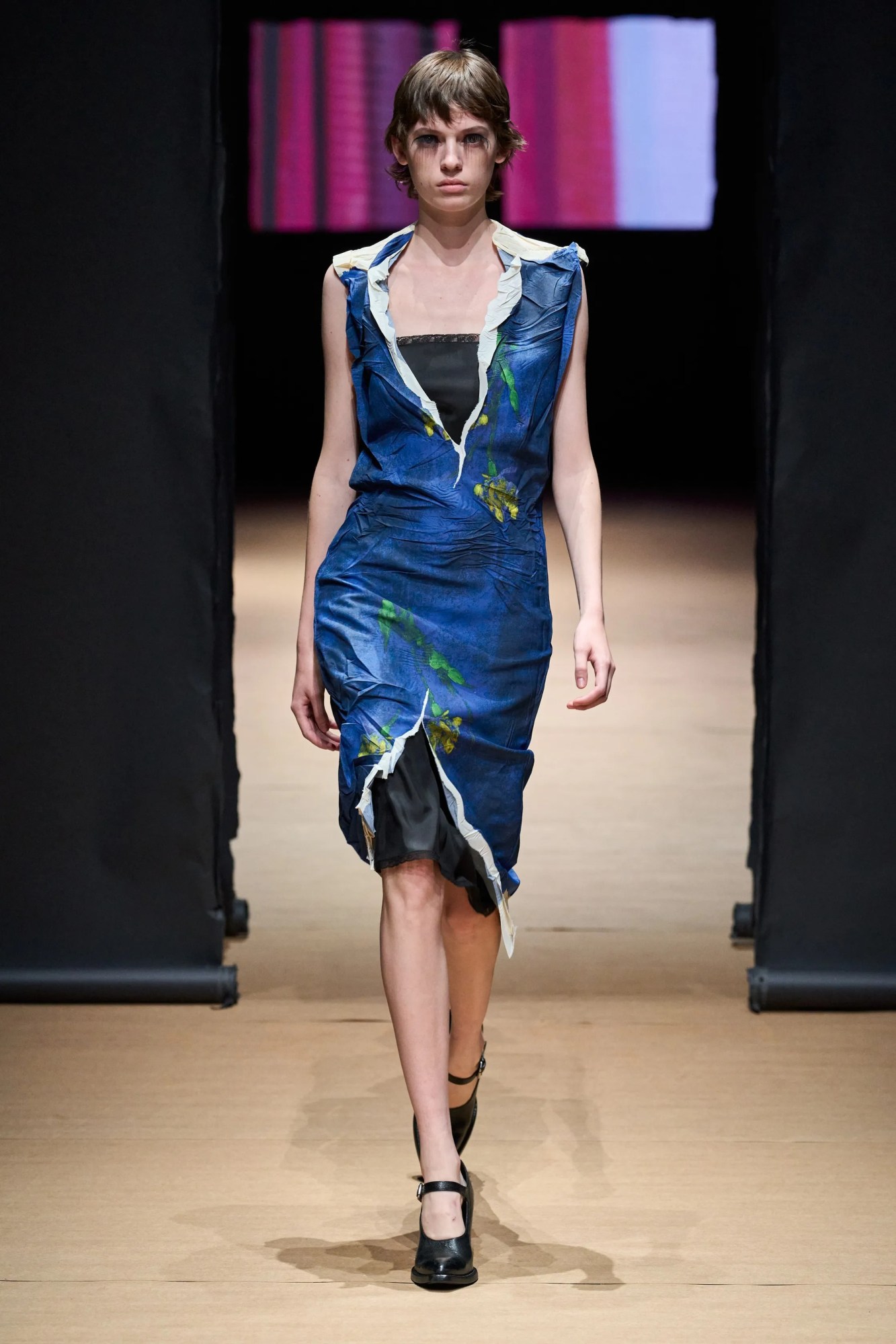 A model walking the Prada SS23 runway in a blue-painted, torn paper dress