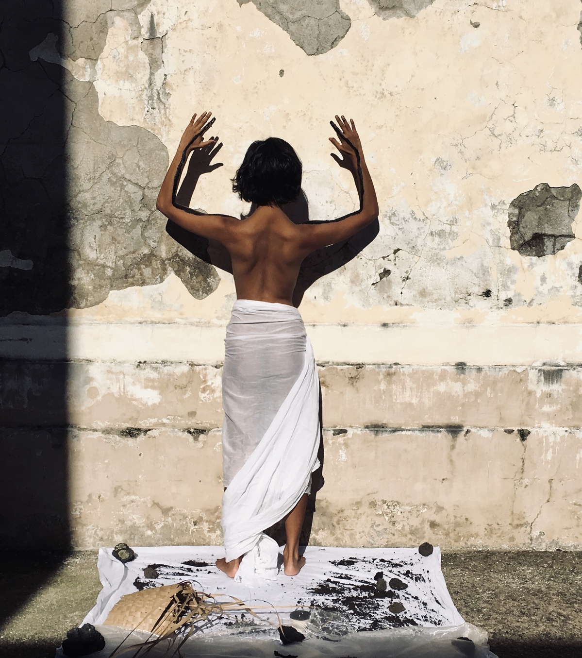 a woman in a white sarong stands with her hands against the wall and back to the camera