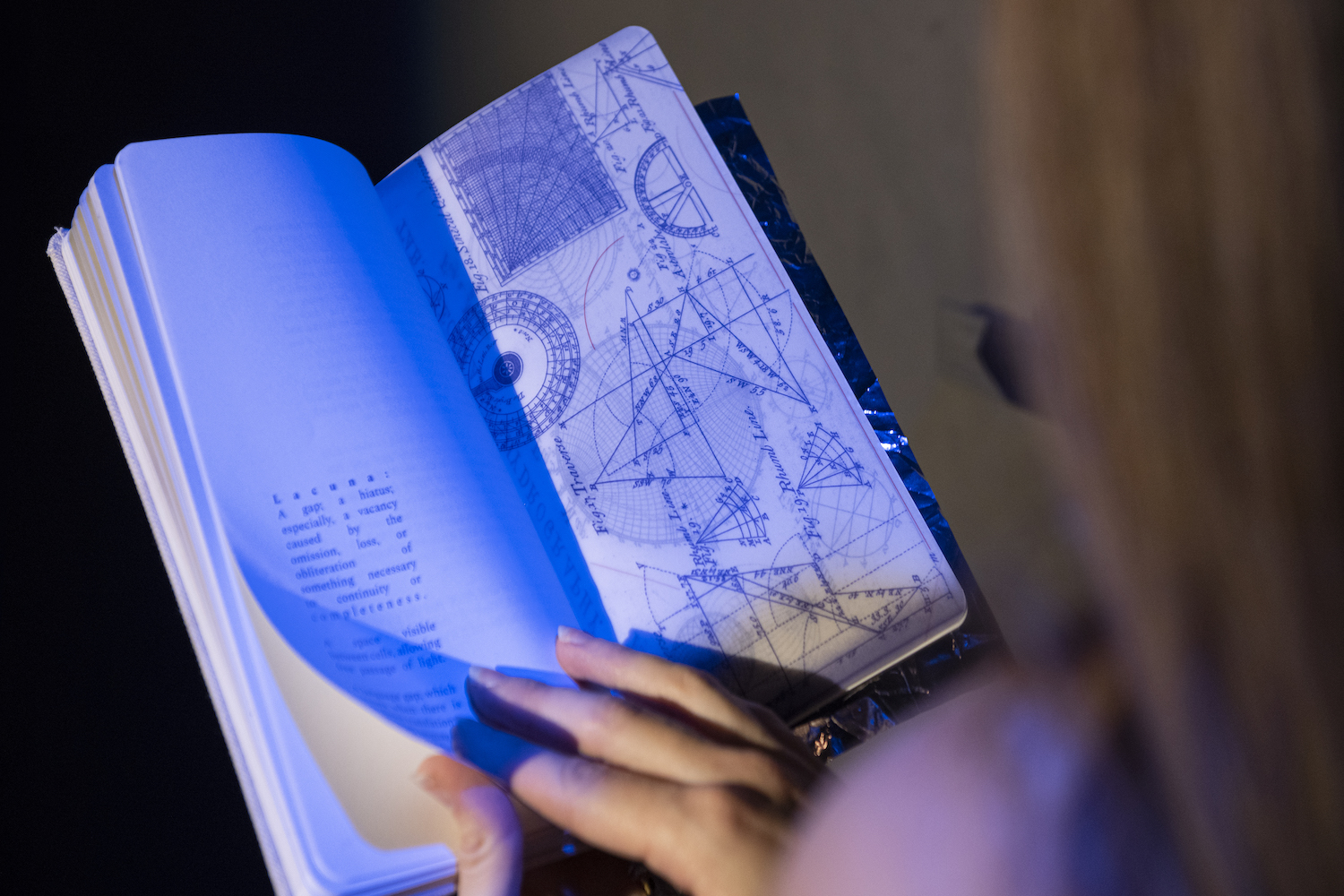 a woman reading a book with drawings and diagrams her face out of shot