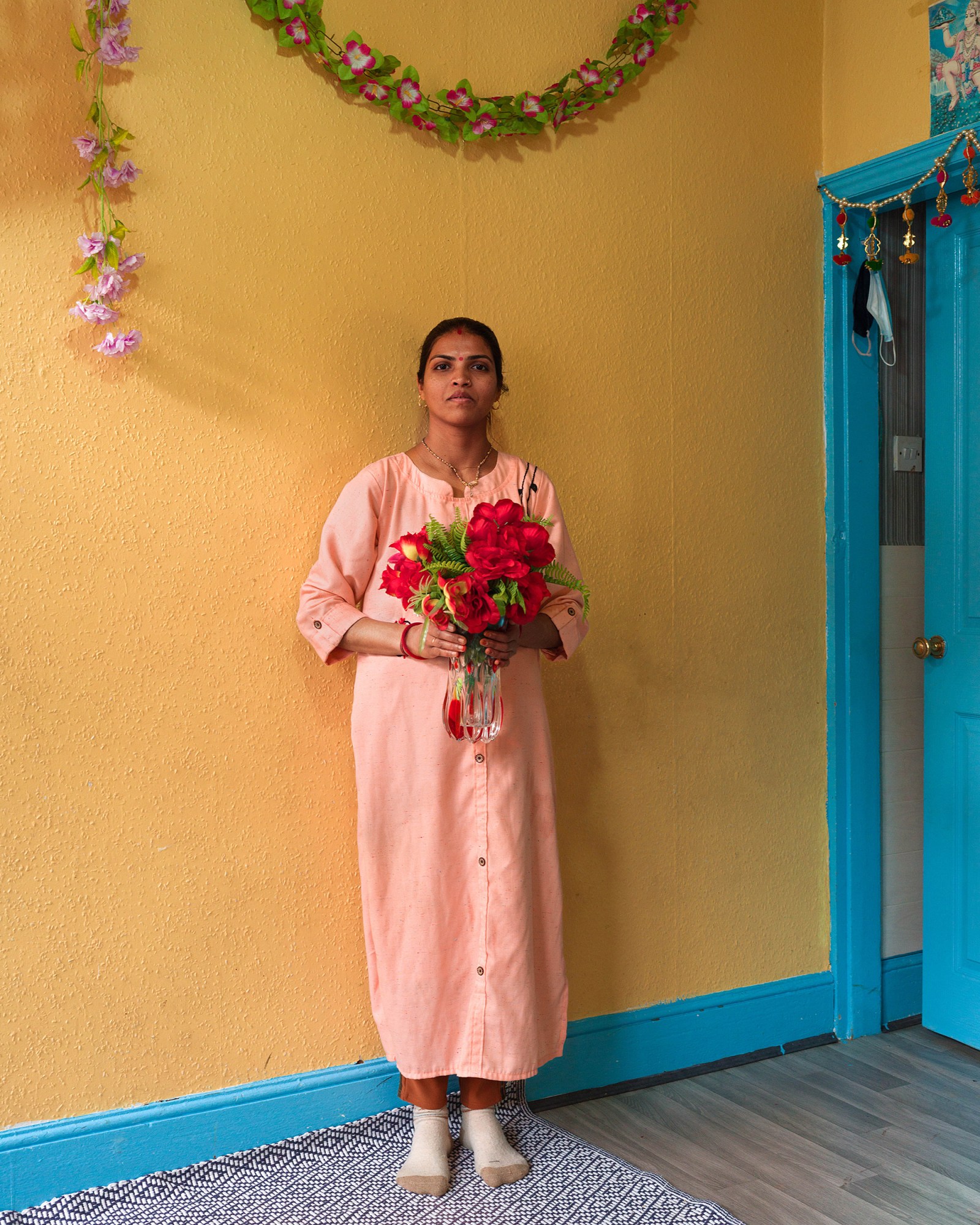 a woman holding red flowers in front of a yellow wall