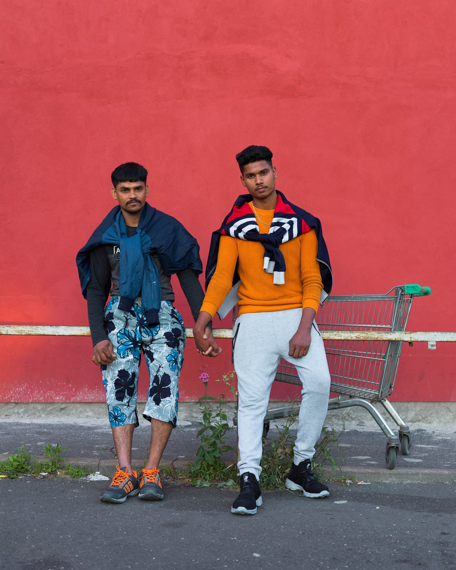 two young men holding hands in front of a red wall