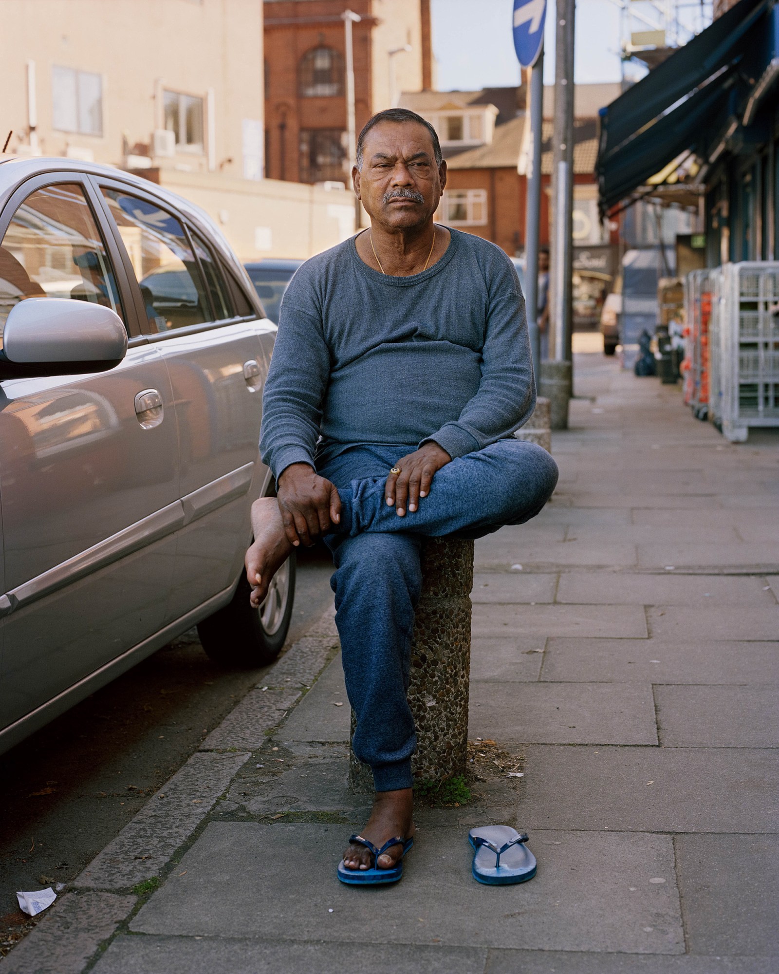 a man in flip flops sitting on a contrete stool on the sidewalk