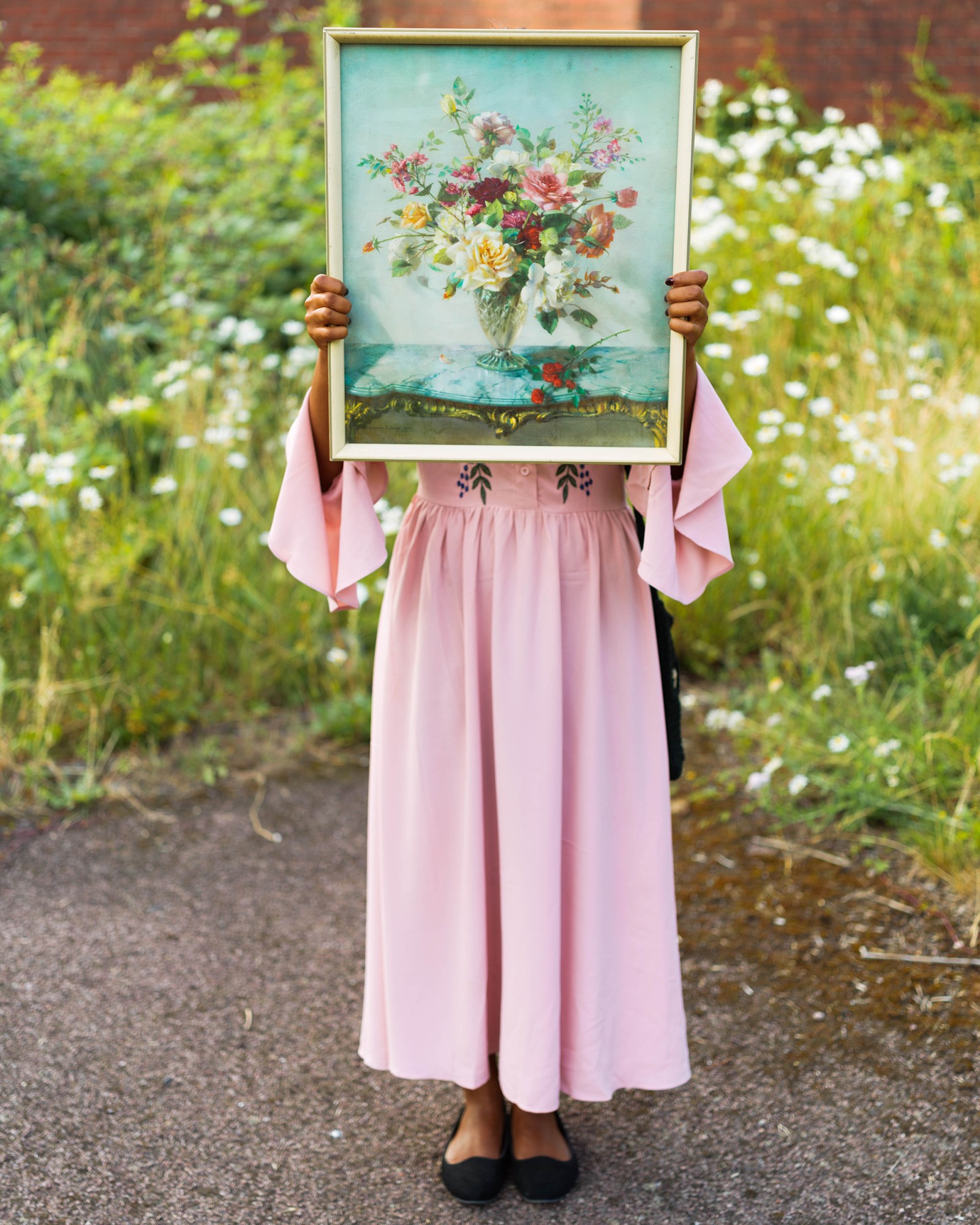 a young woman holding a painting of flowers in front of a field of flowers while wearing a pink dress