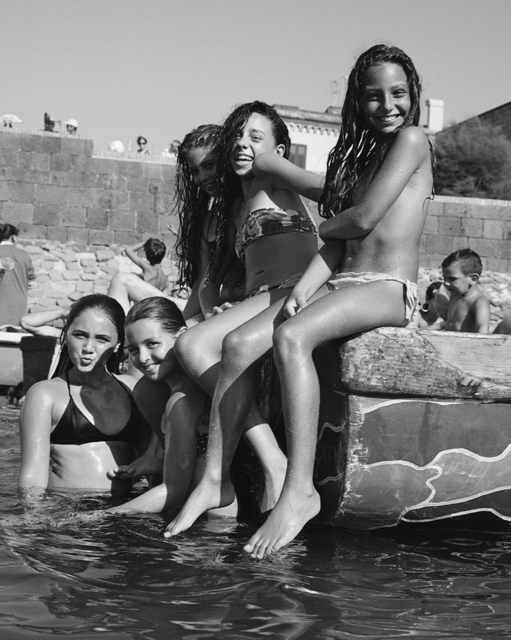 a group of young girls sitting by the sea smile at the camera