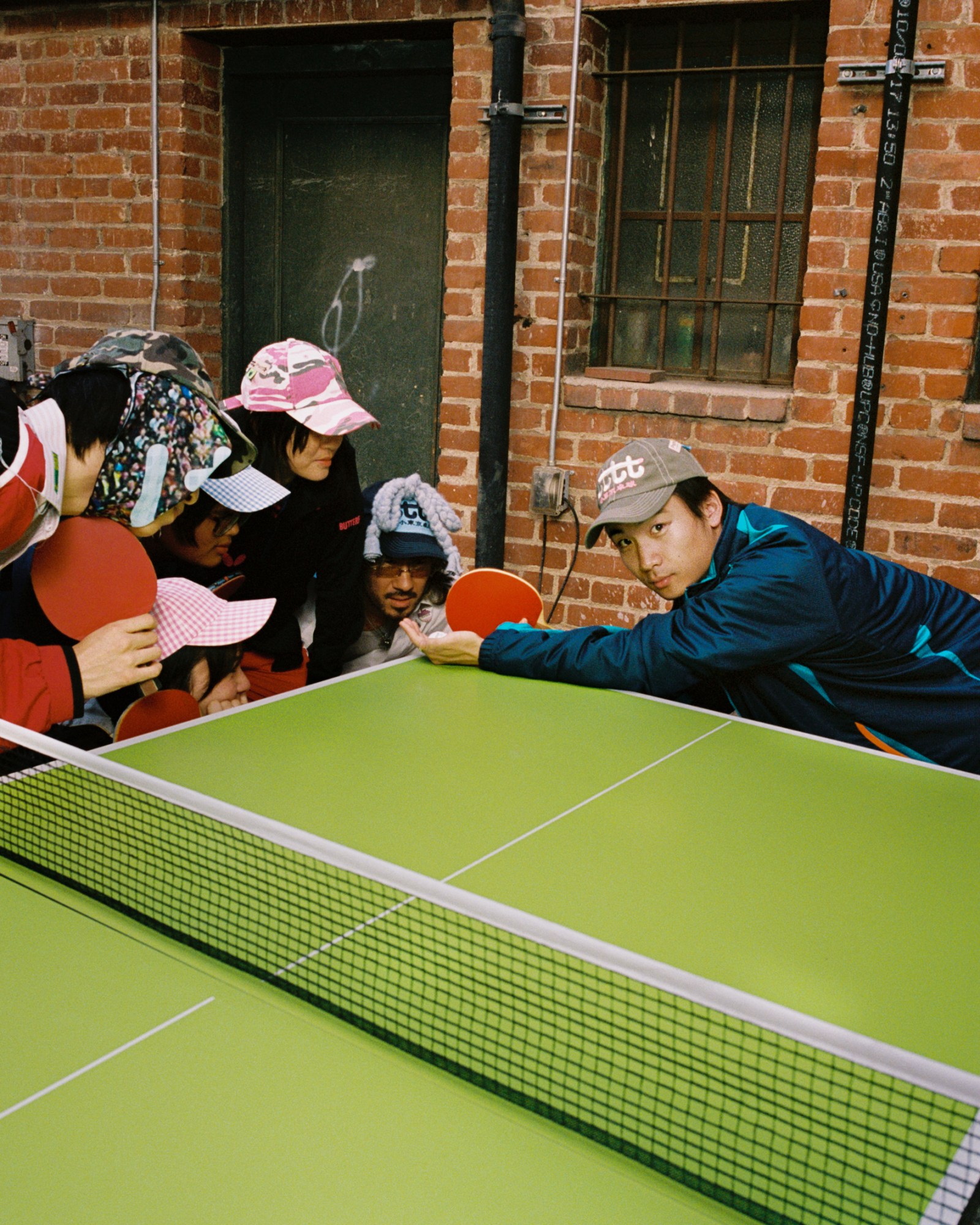 ethan ming reaching across a ping-pong table and looking into the camera