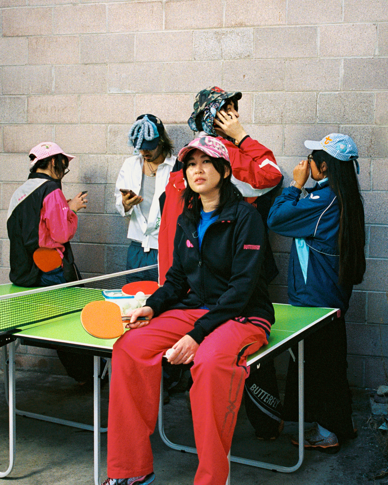 a group of people standing in front of a ping-pong table that susan kounlavongsa is sitting on