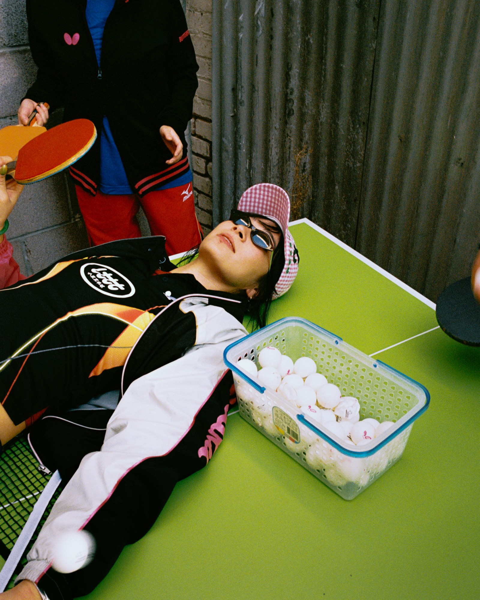 a girl in a hat and sunglasses lying on a bright green ping-pong table