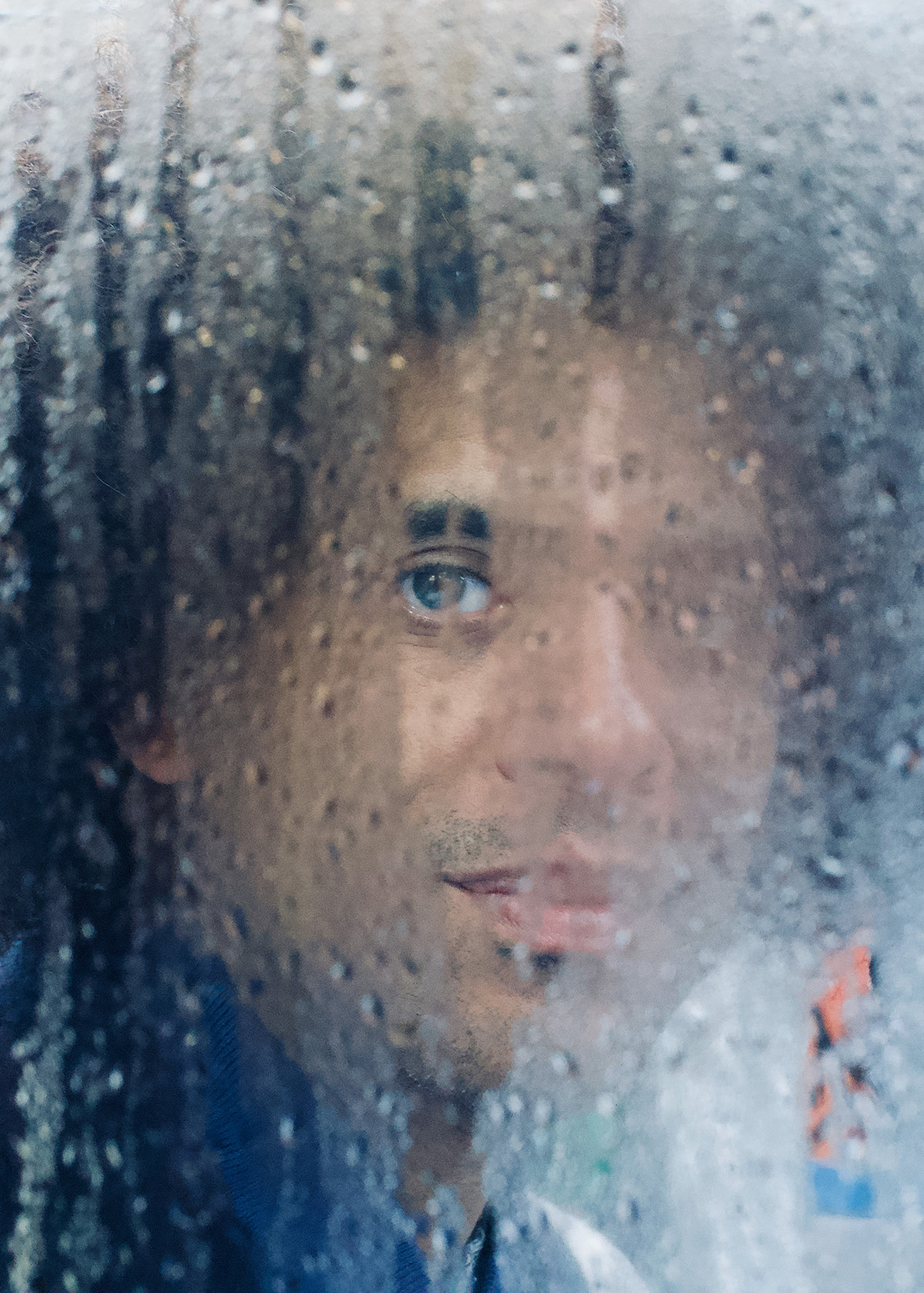 A man looks through a rainy window at the camera.