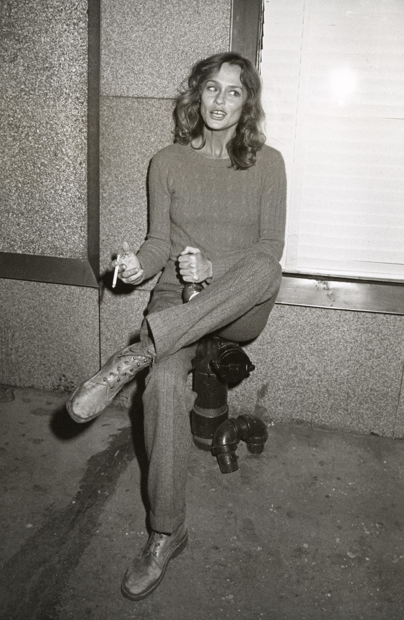 lauren hutton sitting on a chair on a sidewalk holding a beer and cigarette 1981