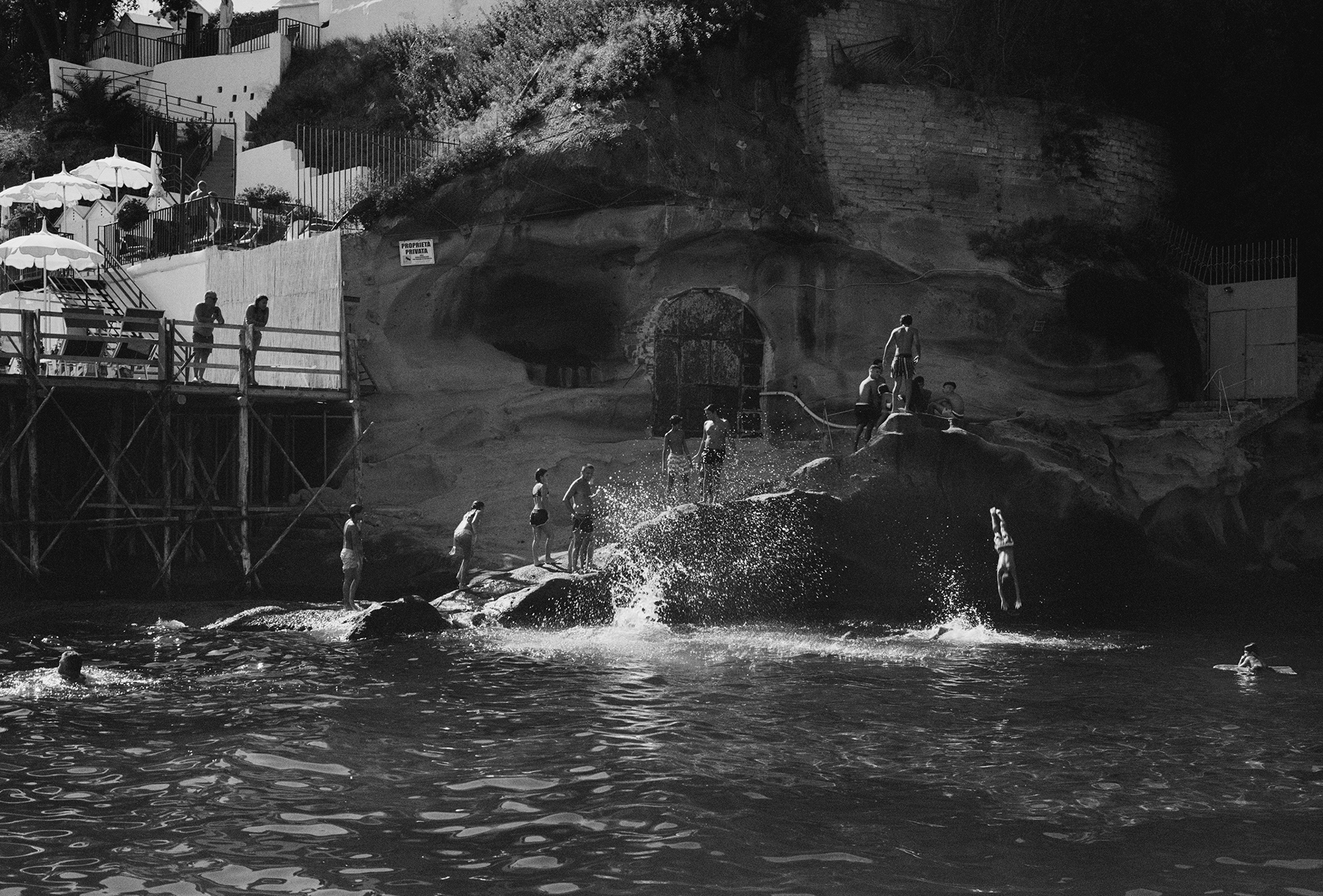 people are pictured jumping from rocks into the sea in a rocky cove