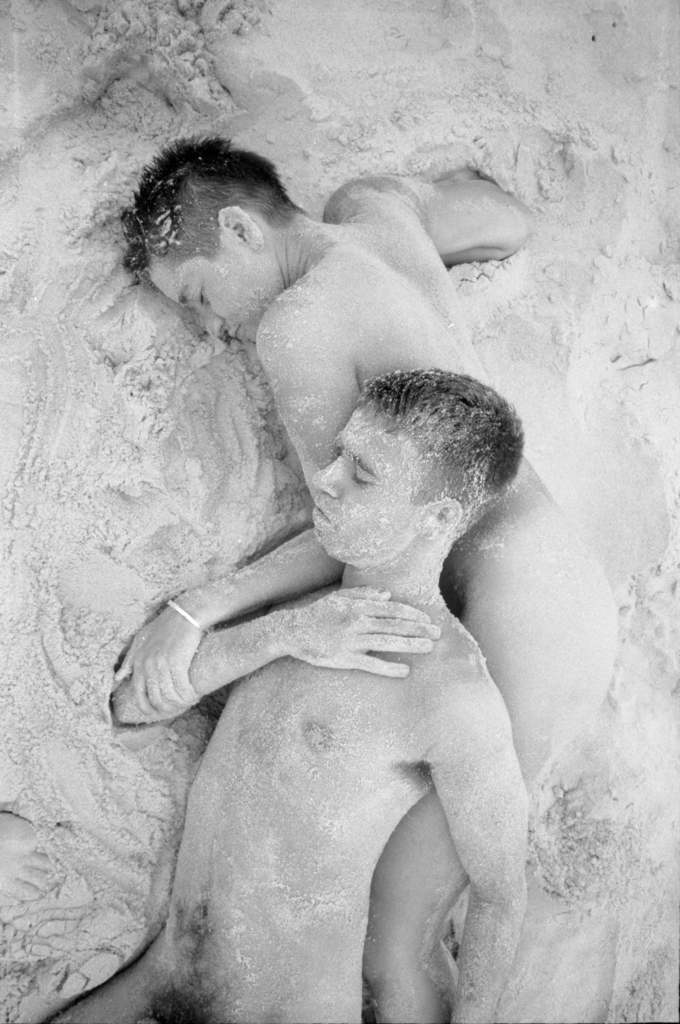 ​Two people lying naked in the sand.