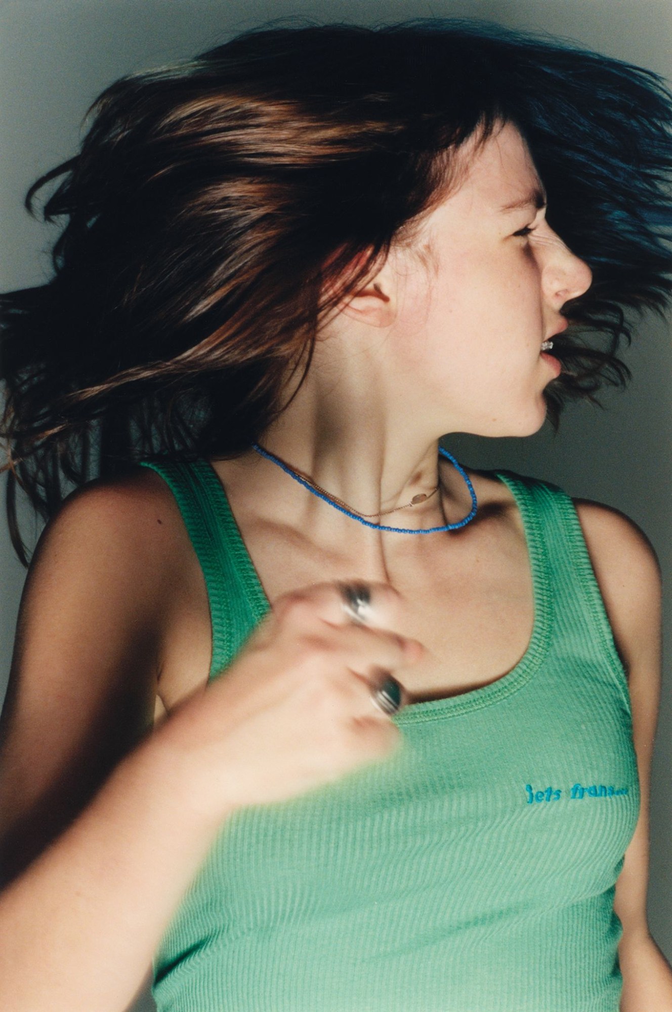 a teen with braces and a green tank top shakes her hair from side to side