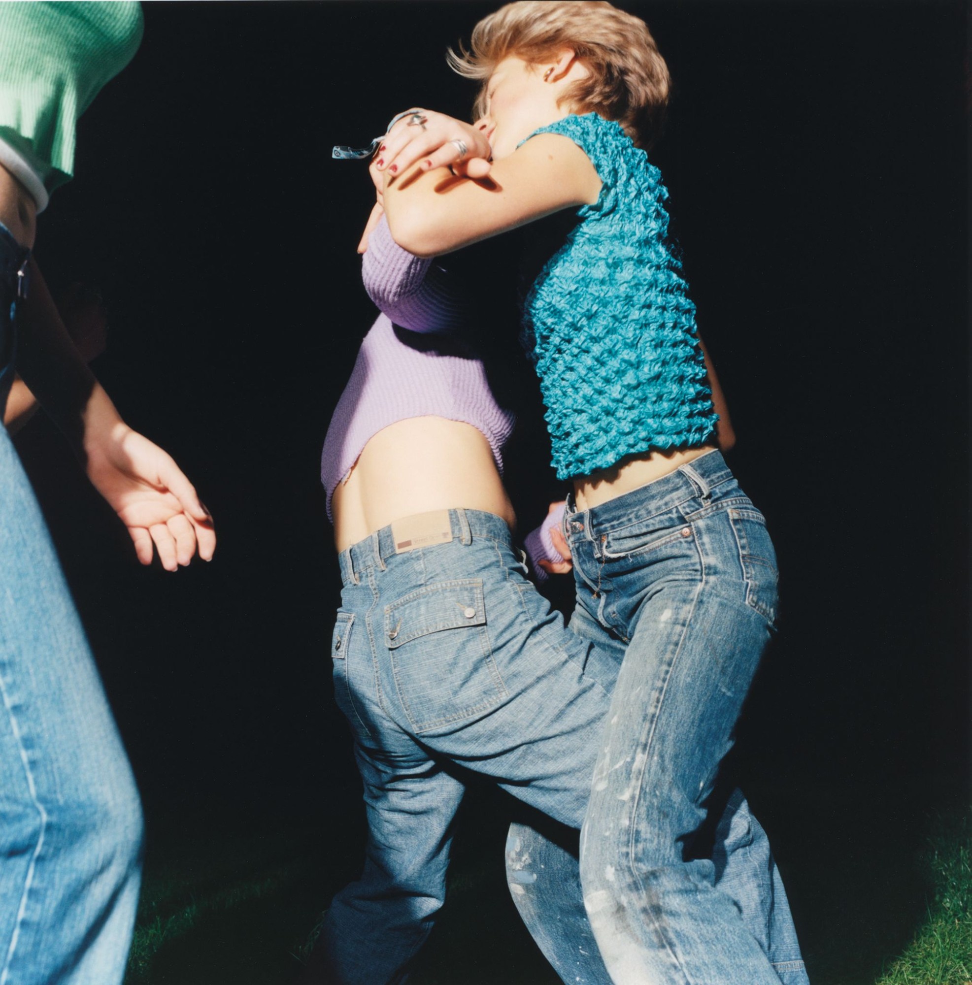 a group of teen girls wearing jeans and colourful tops captured dancing in a dark garden