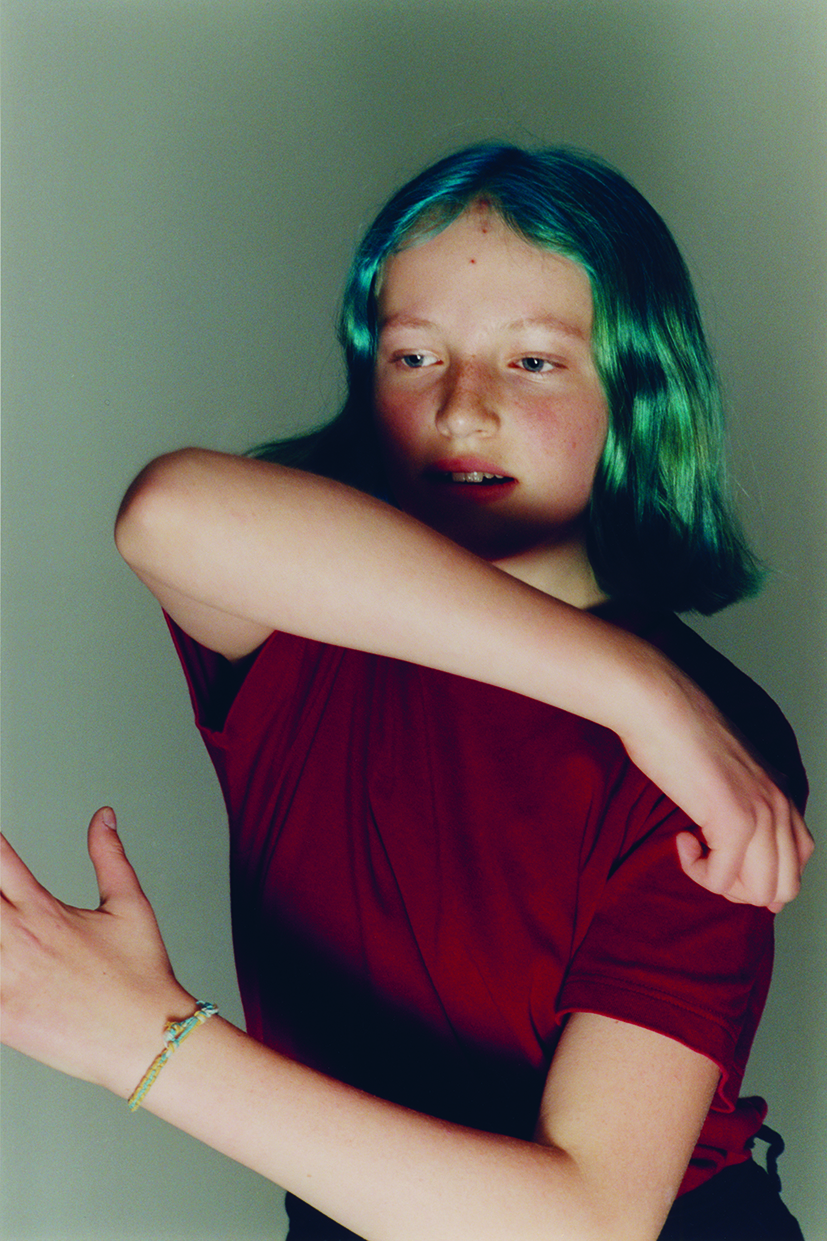 a teen with bright blue hair moves about in a studio