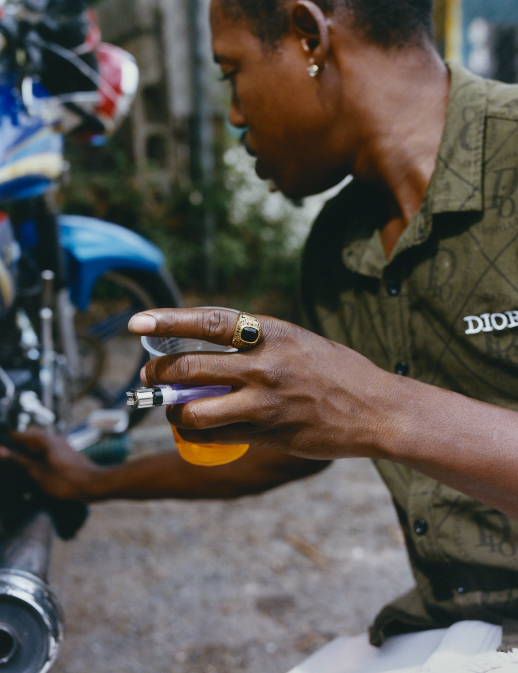 A Jamaican artist with a drink and a lighter looking at a motorbike photographed by Jeano Edwards for i-D’s The Royalty Issue, no. 370, Winter 2022