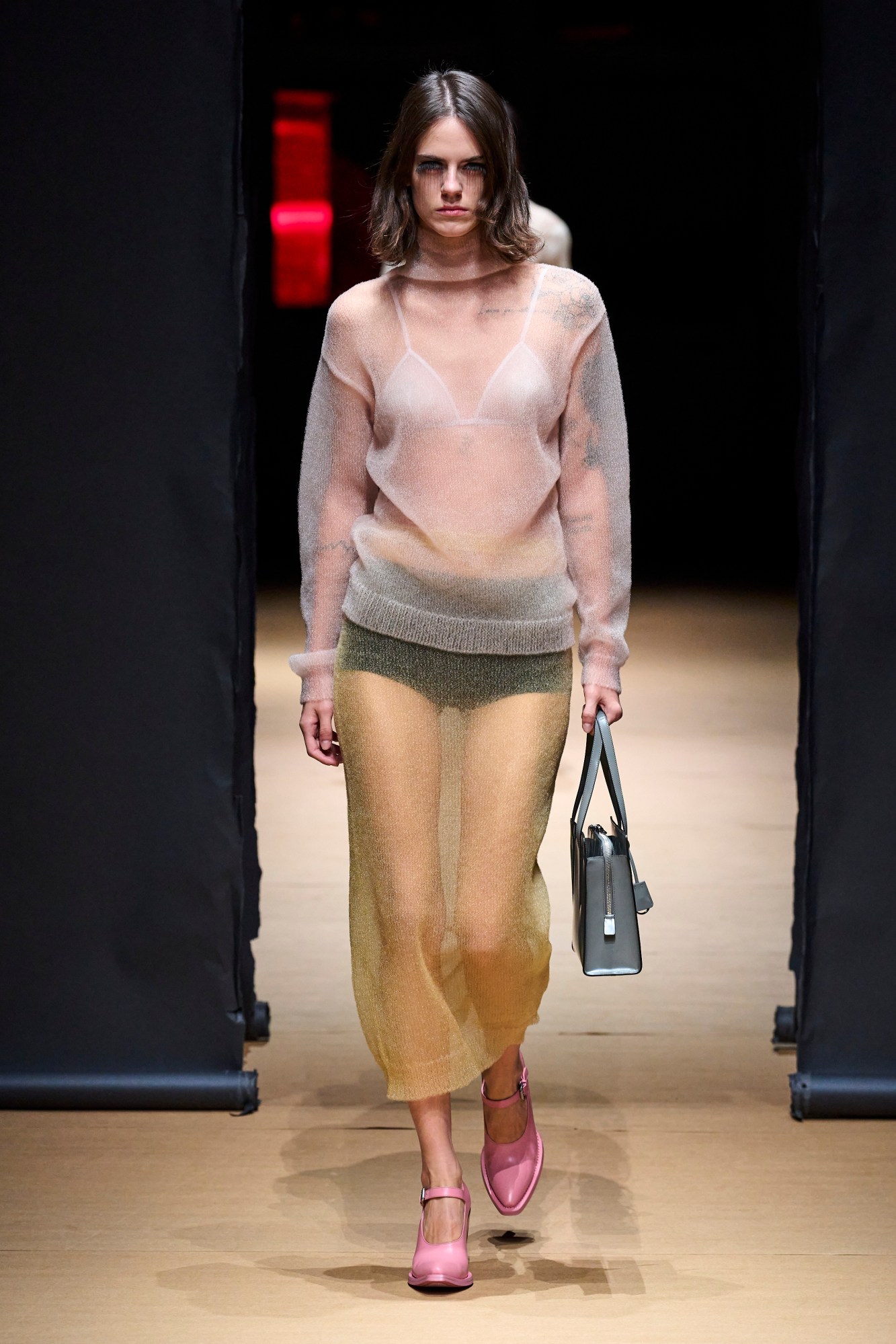 A model walking the runway at Milan Fashion Week wearing a seethrough jumper and skirt