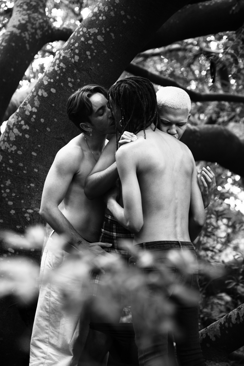 three people kissing amongst trees