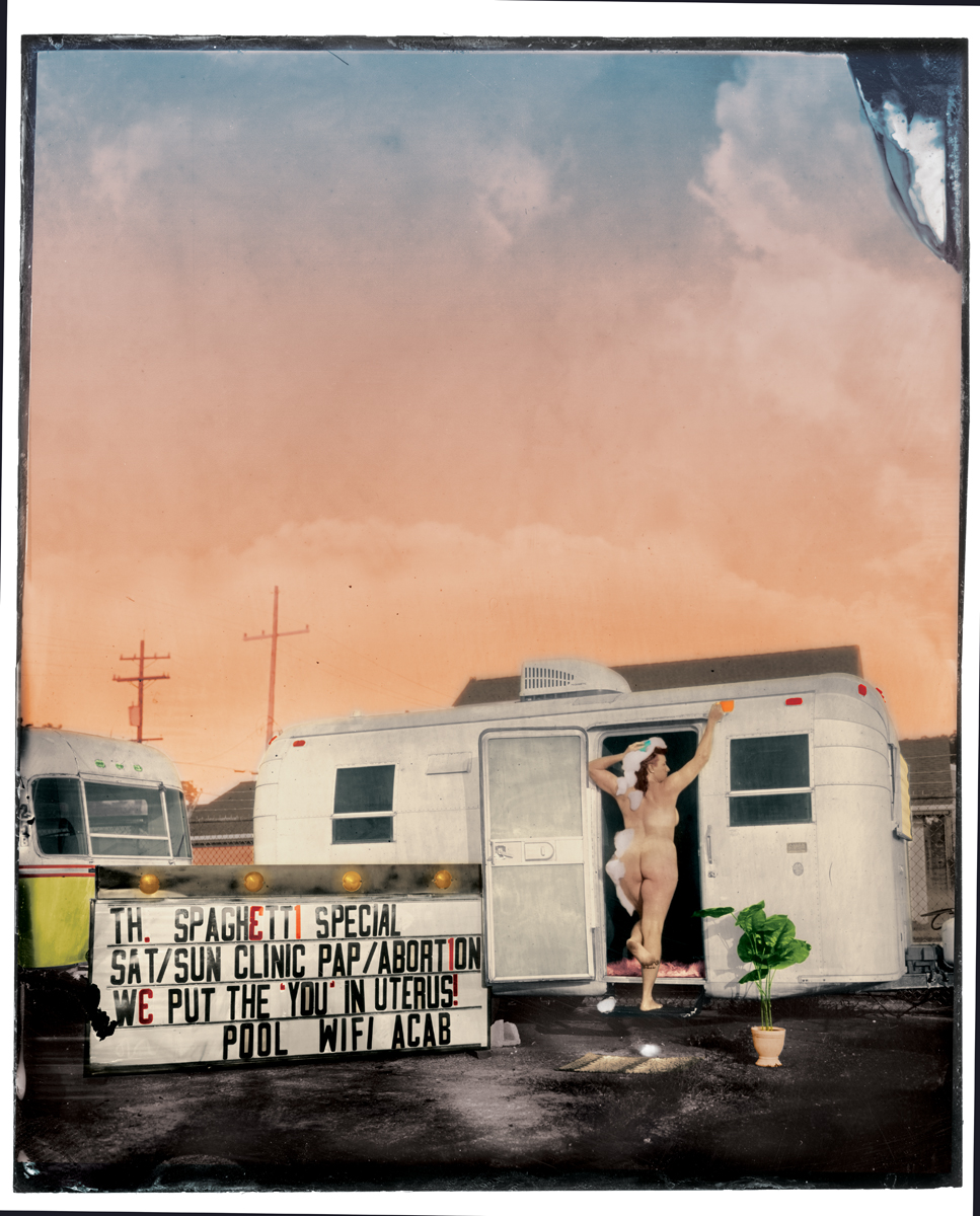 a naked woman standing in the doorway of an airstream trailer