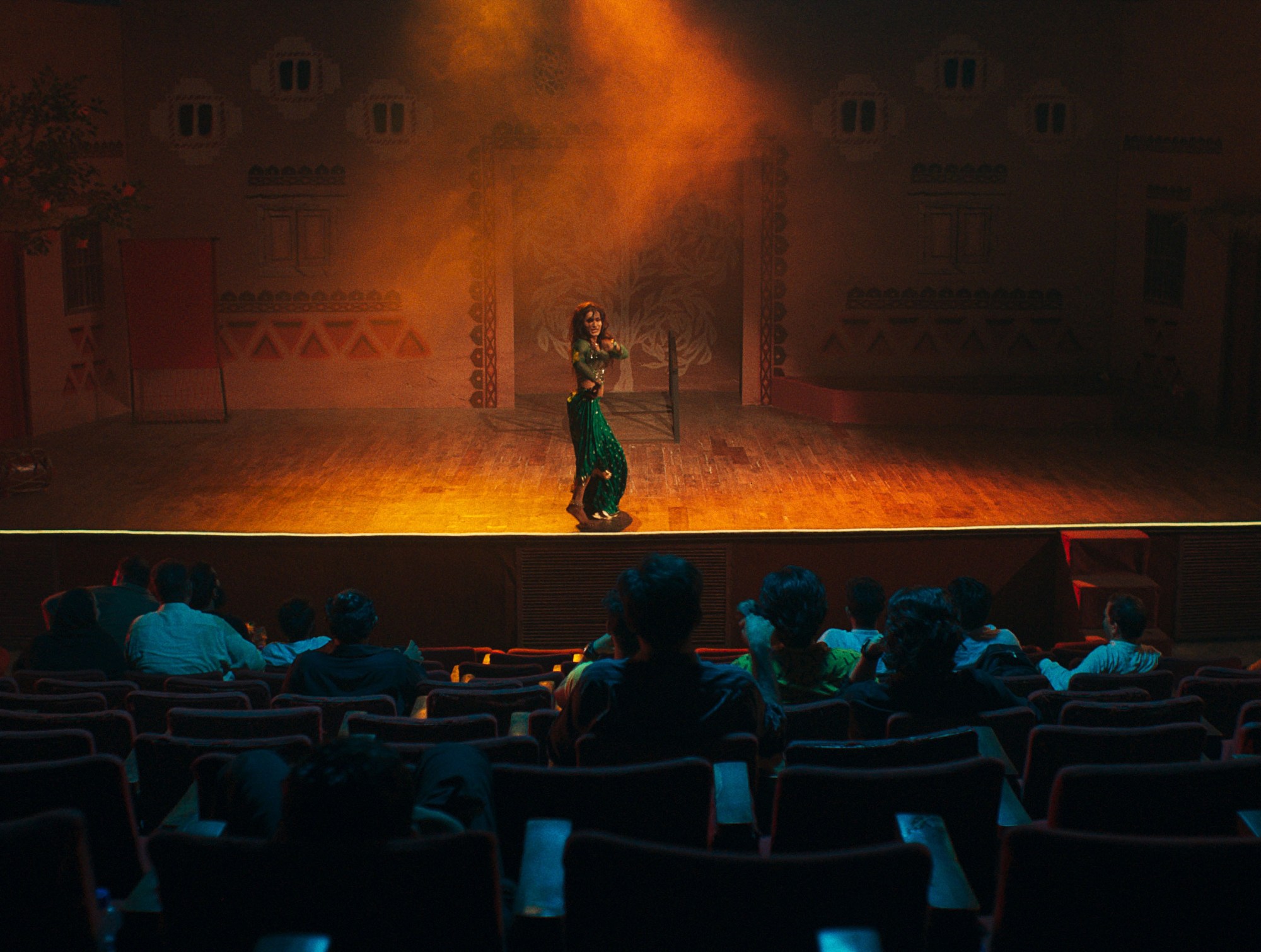 a woman in a green outfit performs for a small audience on a orange-lit stage