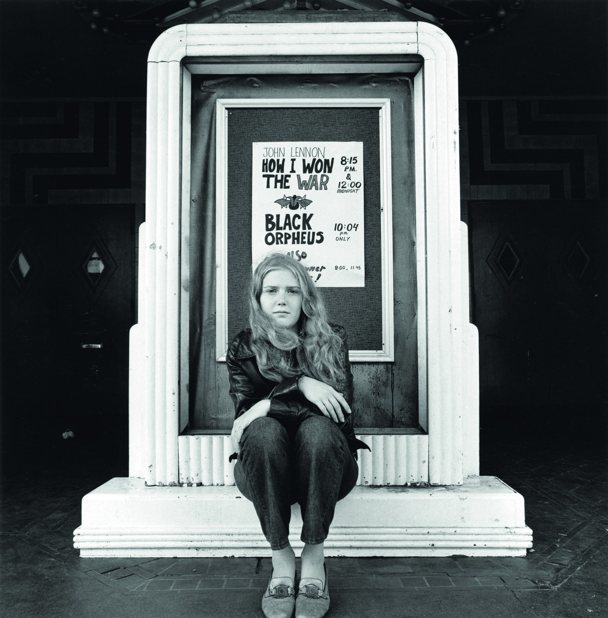 black-and-white image of a young woman sitting outside a cinema