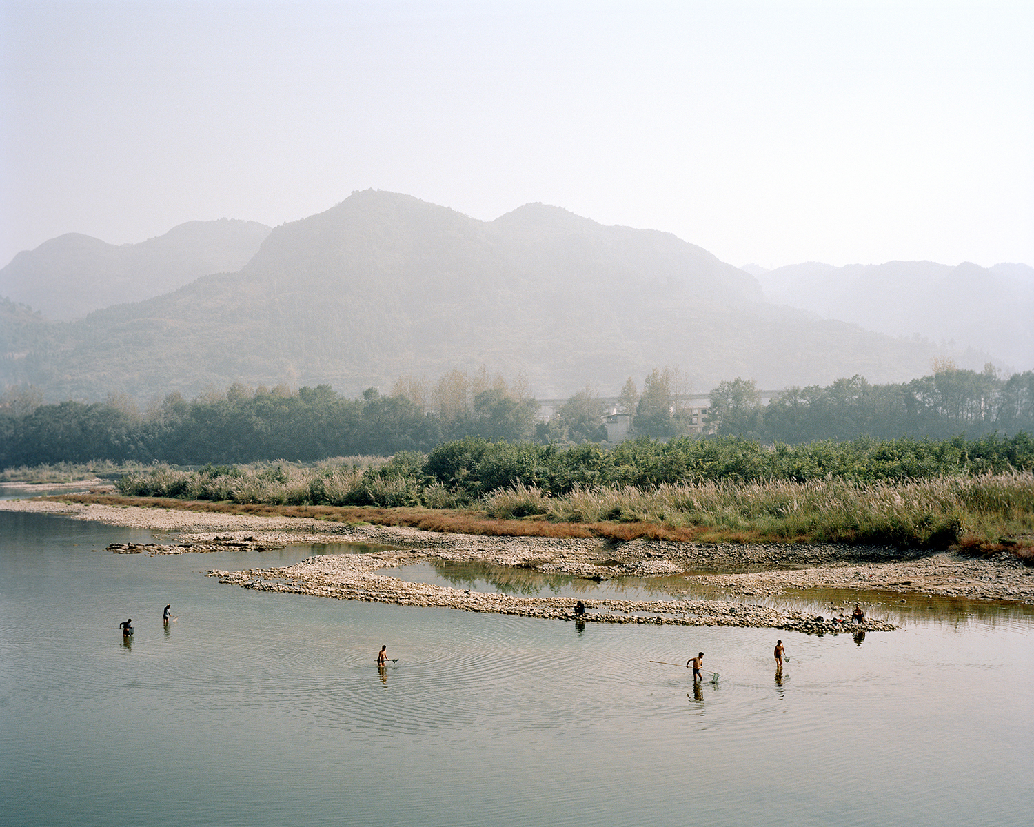 a beautiful scenic shot of people fishing in a wide river, with misty mountains in the background