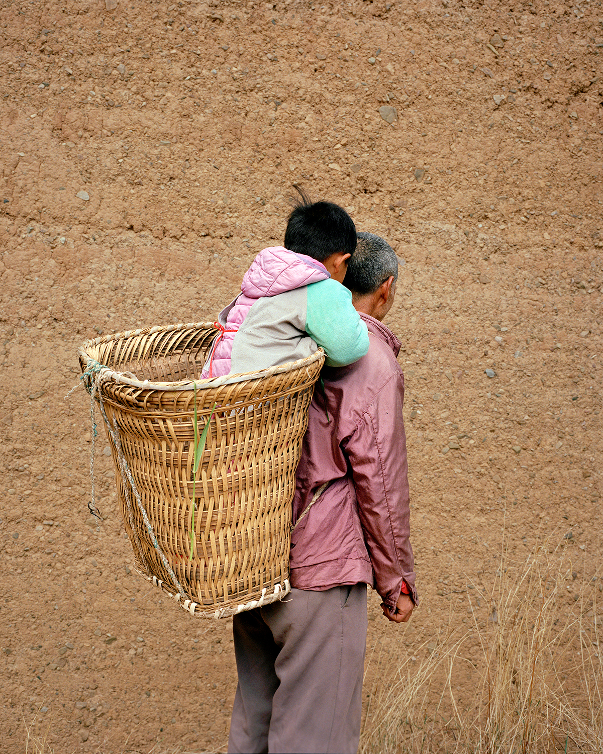 a toddler sits in a woven basket on the shoulders of their grandfather