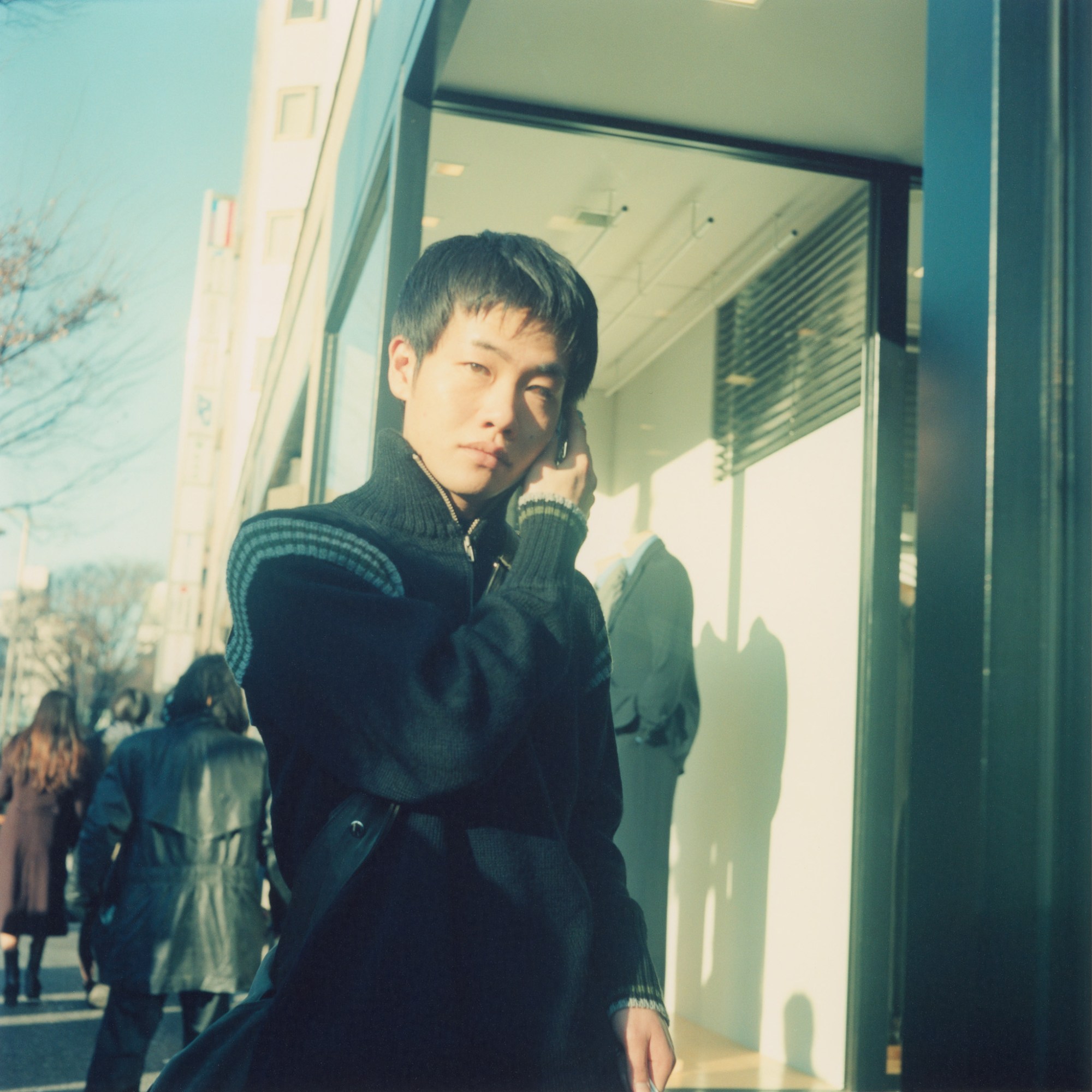 A man holding something to his ear looks into the camera