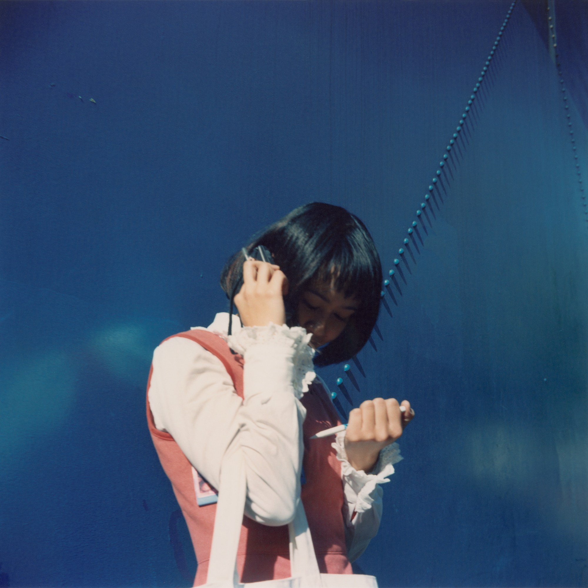 A woman against a blue wall holds something to her ear