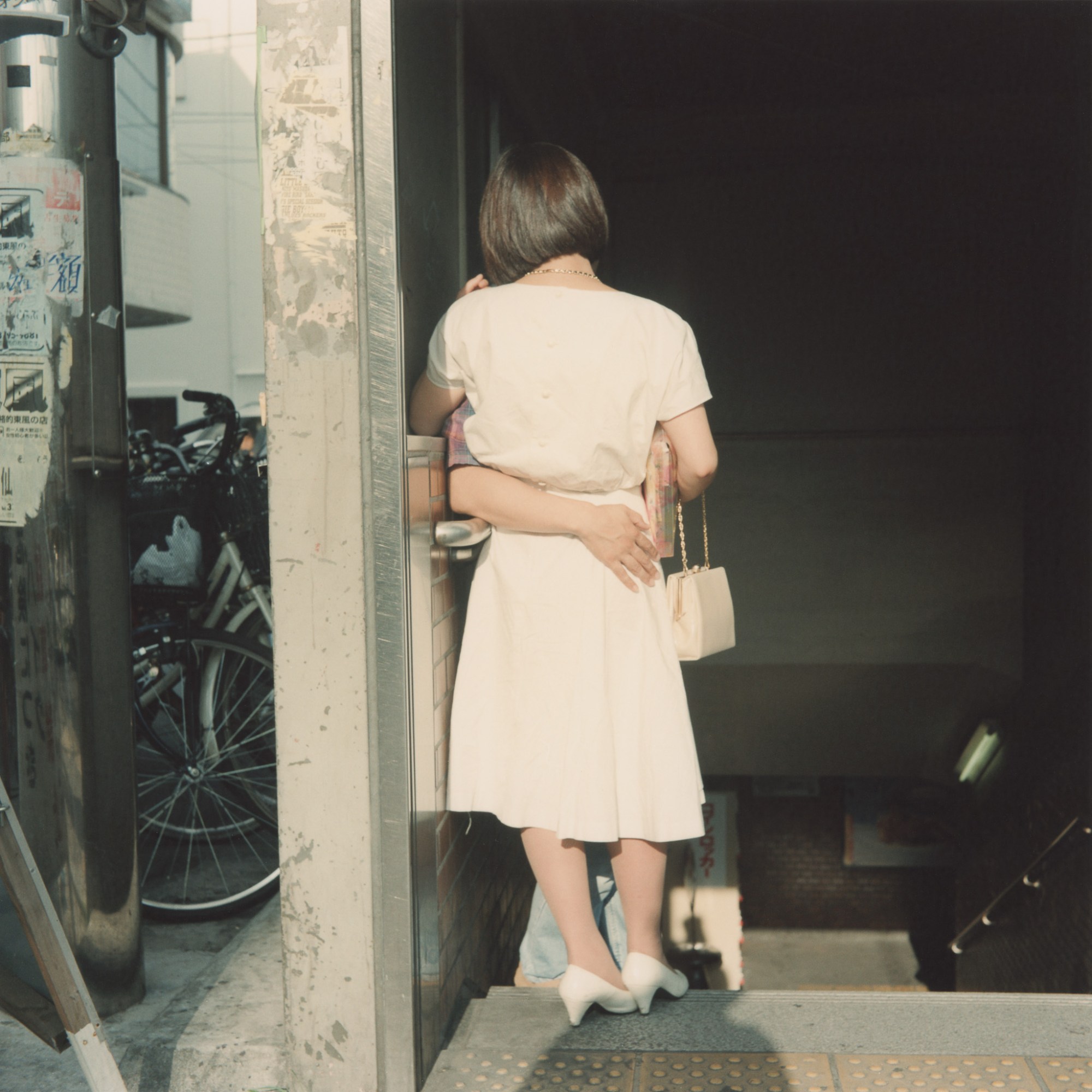 A woman's back at the top of the stairs, a person holds onto her waist