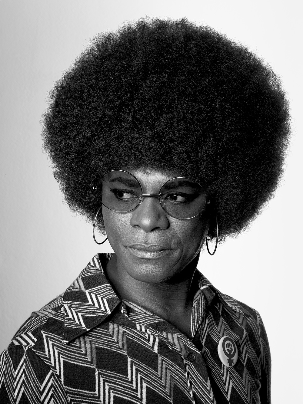 black-and-white portrait of angela davis wearing a geometric print dress, round glasses and hoop earrings