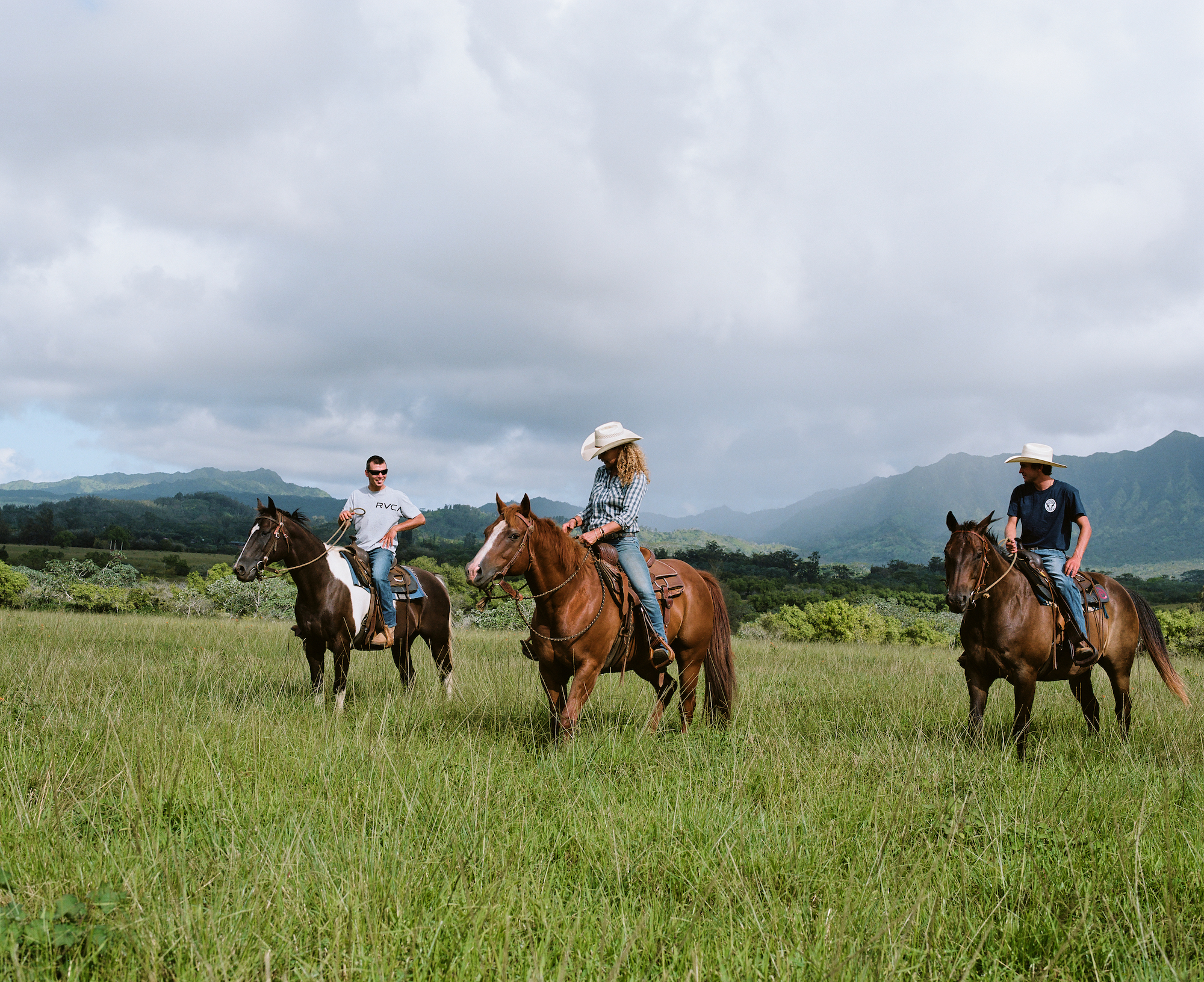 three people riding horses against the backdrop of kaua'i