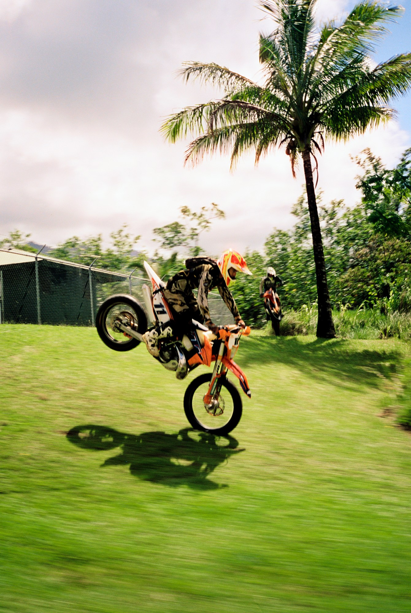 two dirt bike racers against the green grass and palm trees in hawaii