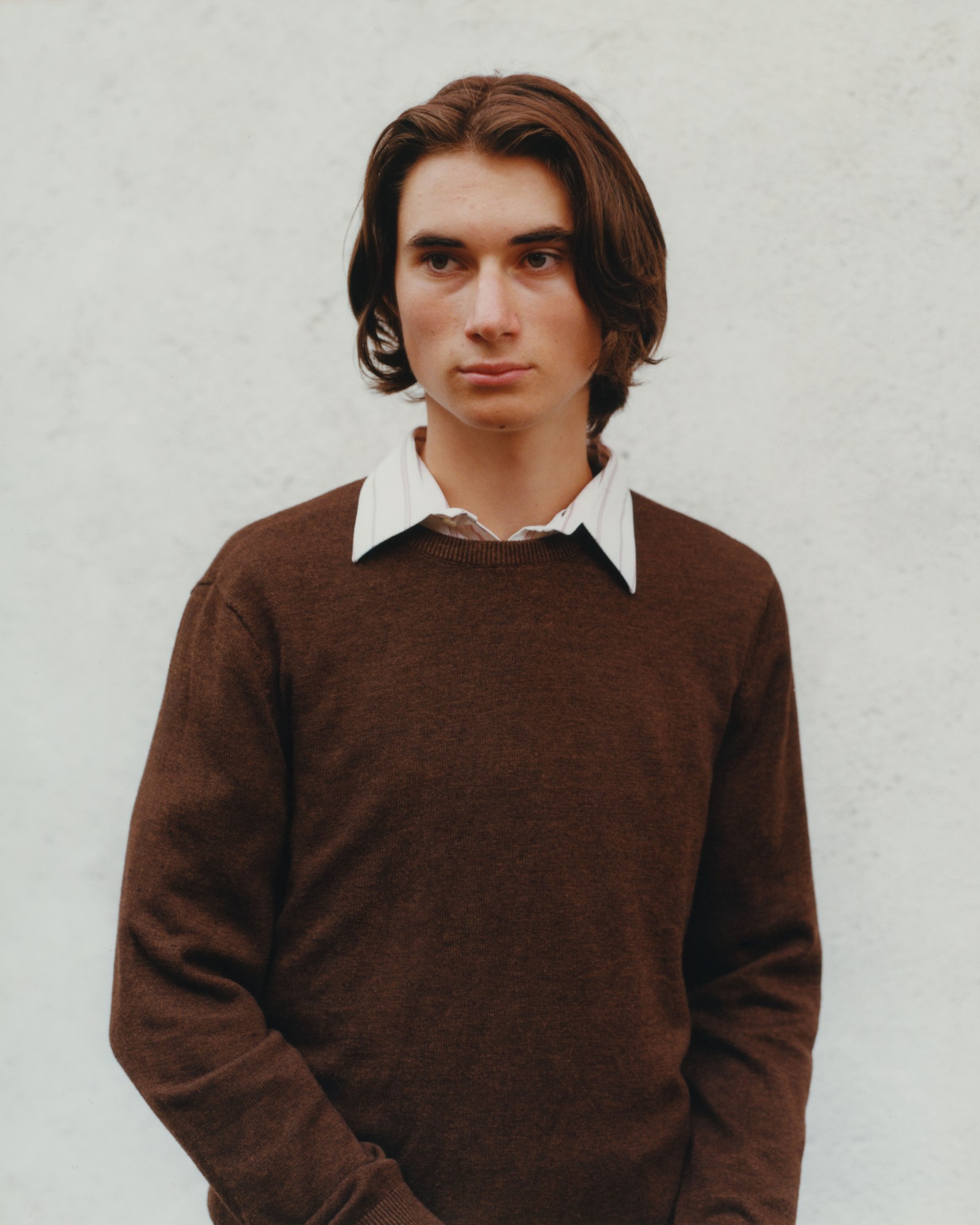 young man in brown jumper shot against a white wall