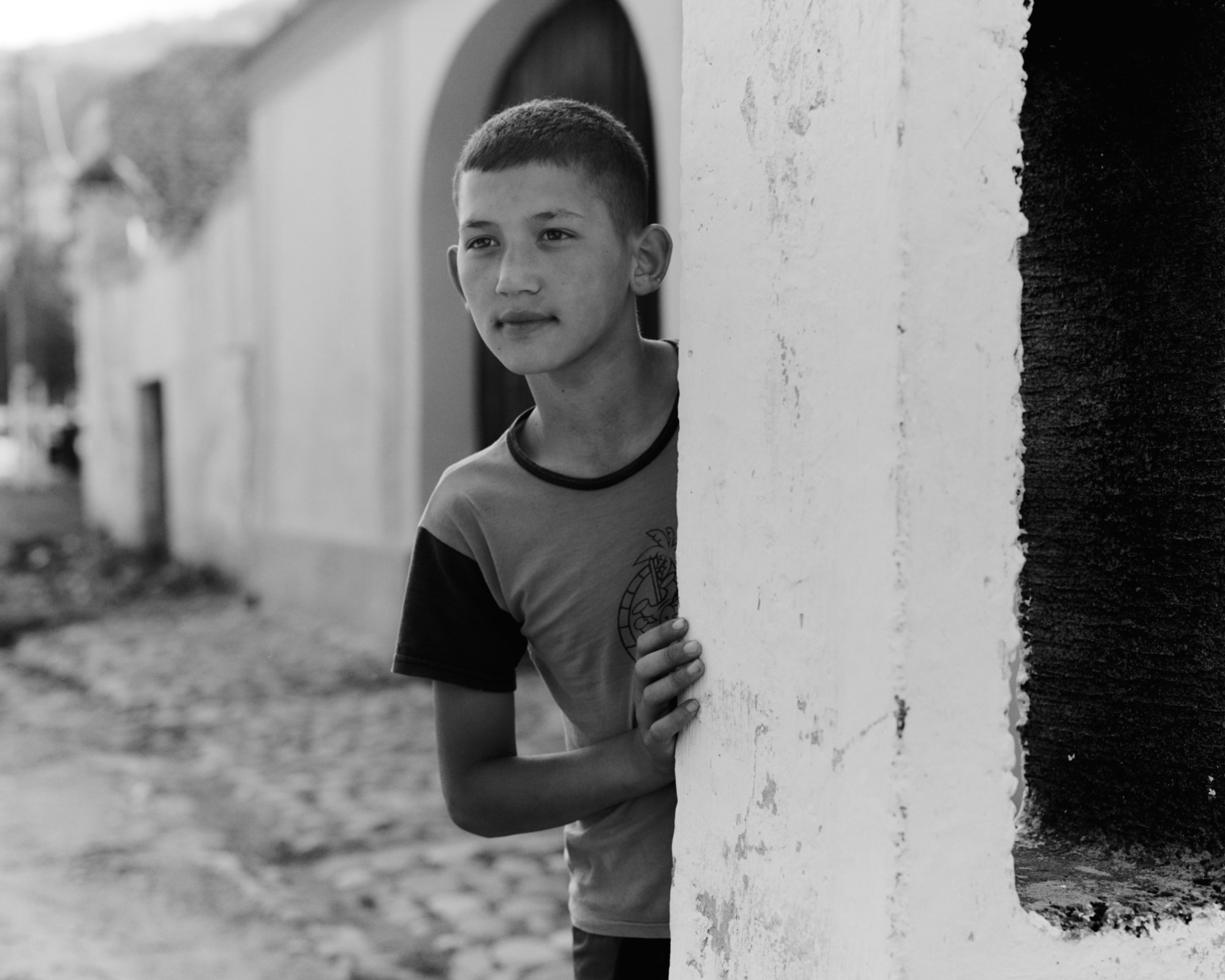 black-and-white image of a young boy in transylvania leaning against a white pillar