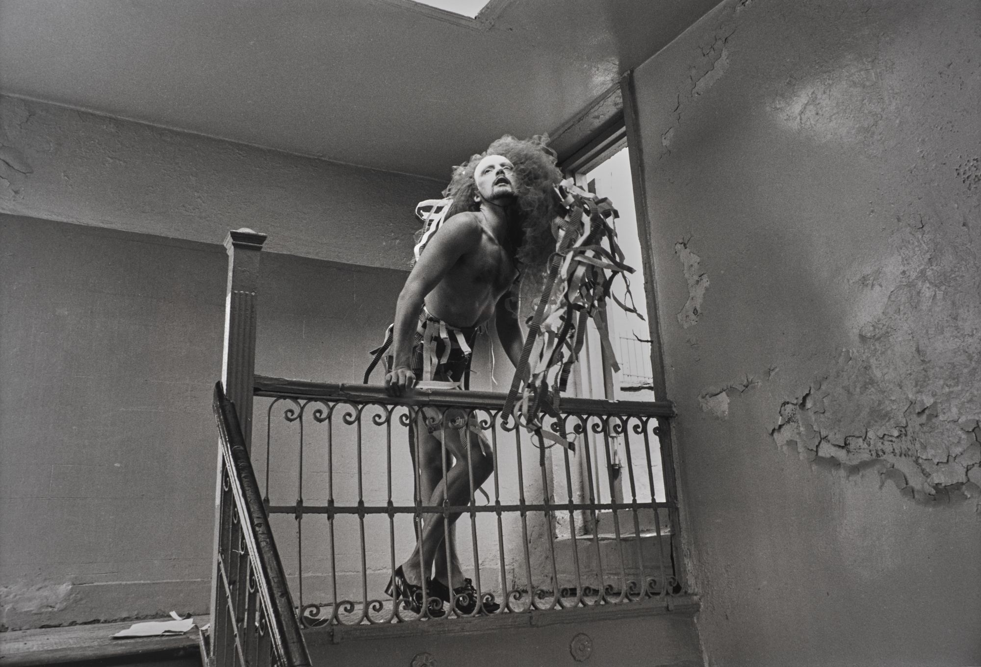 black-and-white image of a man hanging over a bannister in dilapidated apartment block