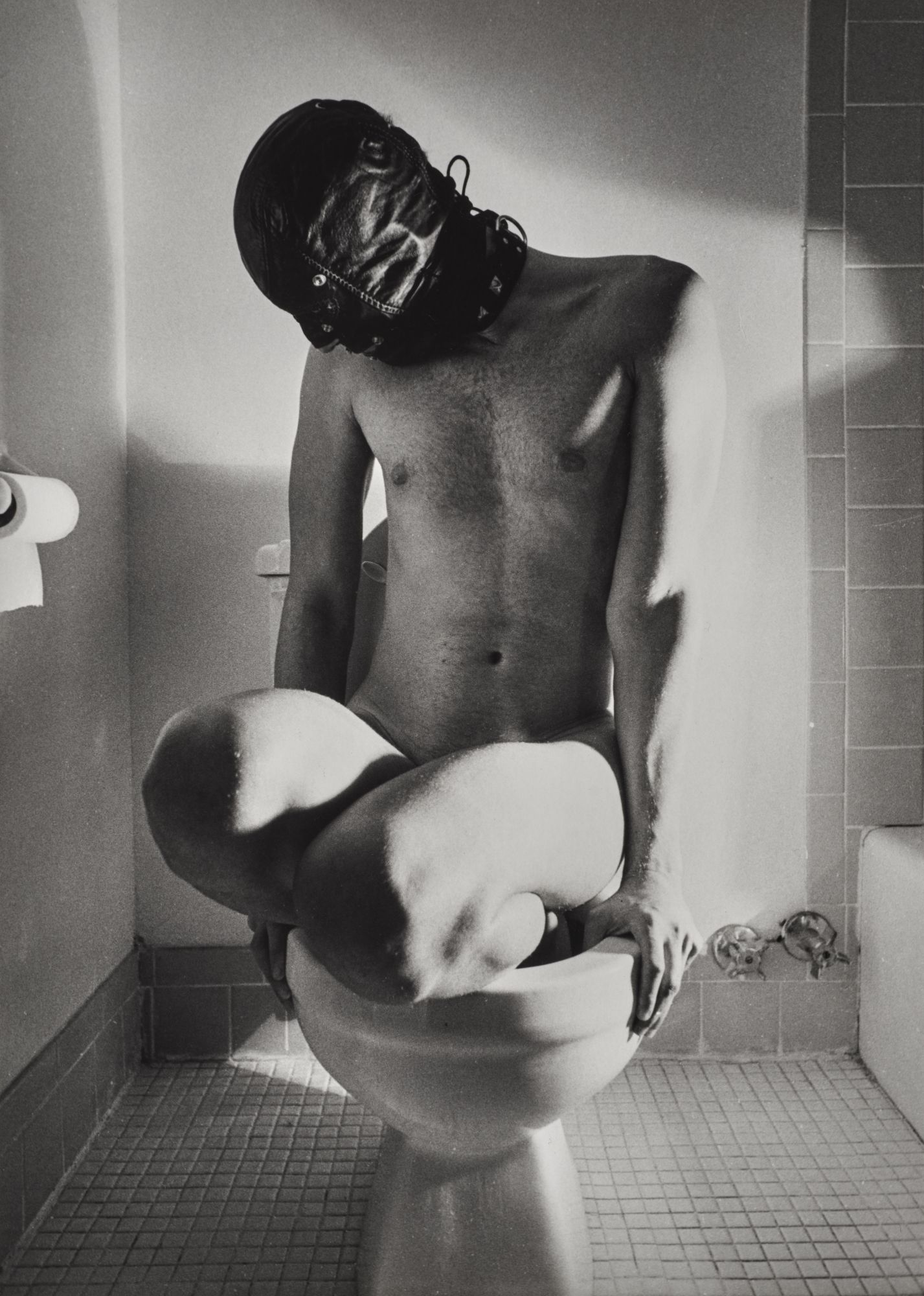 black-and-white image of a man in a gimp mask posing in a toilet bowl