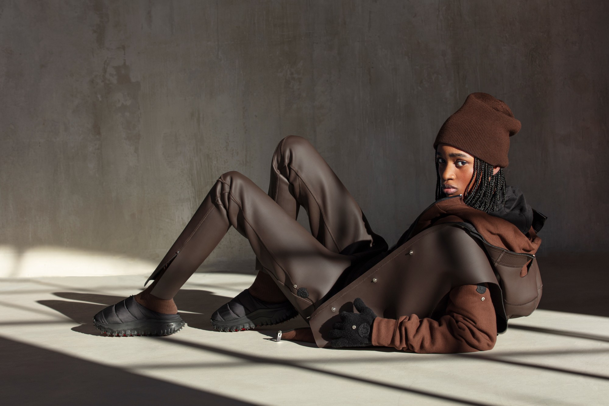 a model reclines on a concrete floor wearing brown outdoorsy clothes