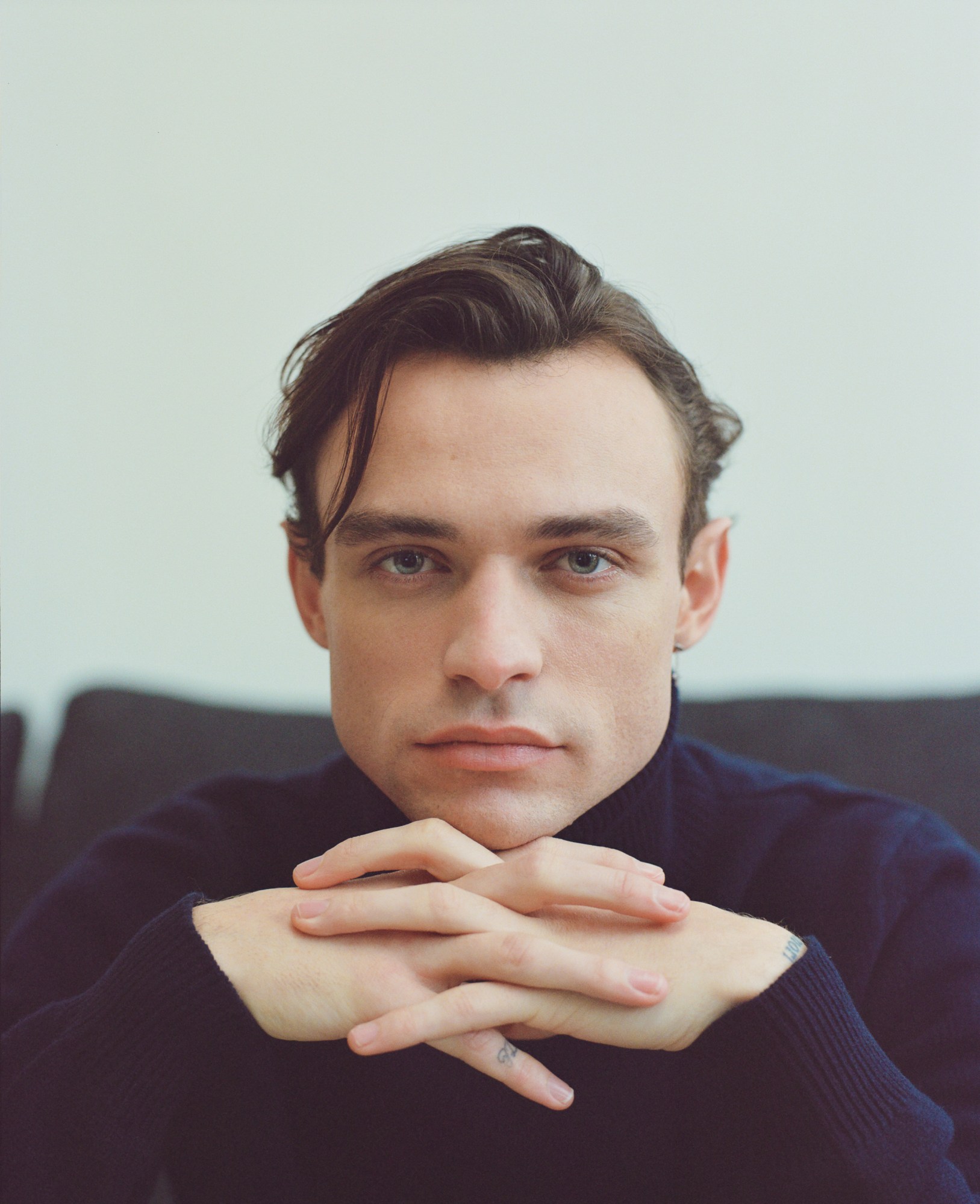 close up portrait of thomas doherty, his chin resting on his linked hands