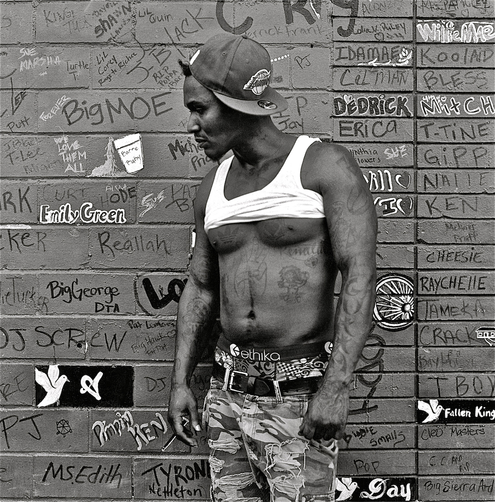 A man with a Lakers hat standing in front of a graffitied wall