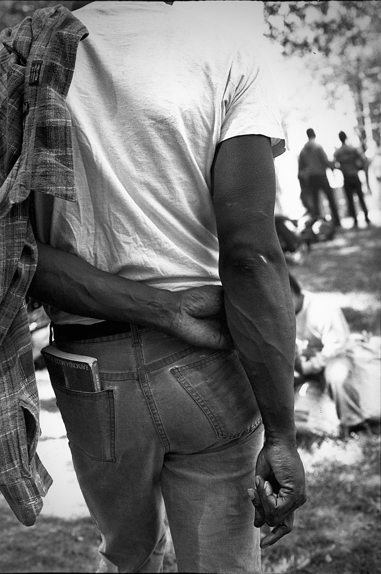 A man with a book in his back pocket and a fleece hanging over his arm leaning